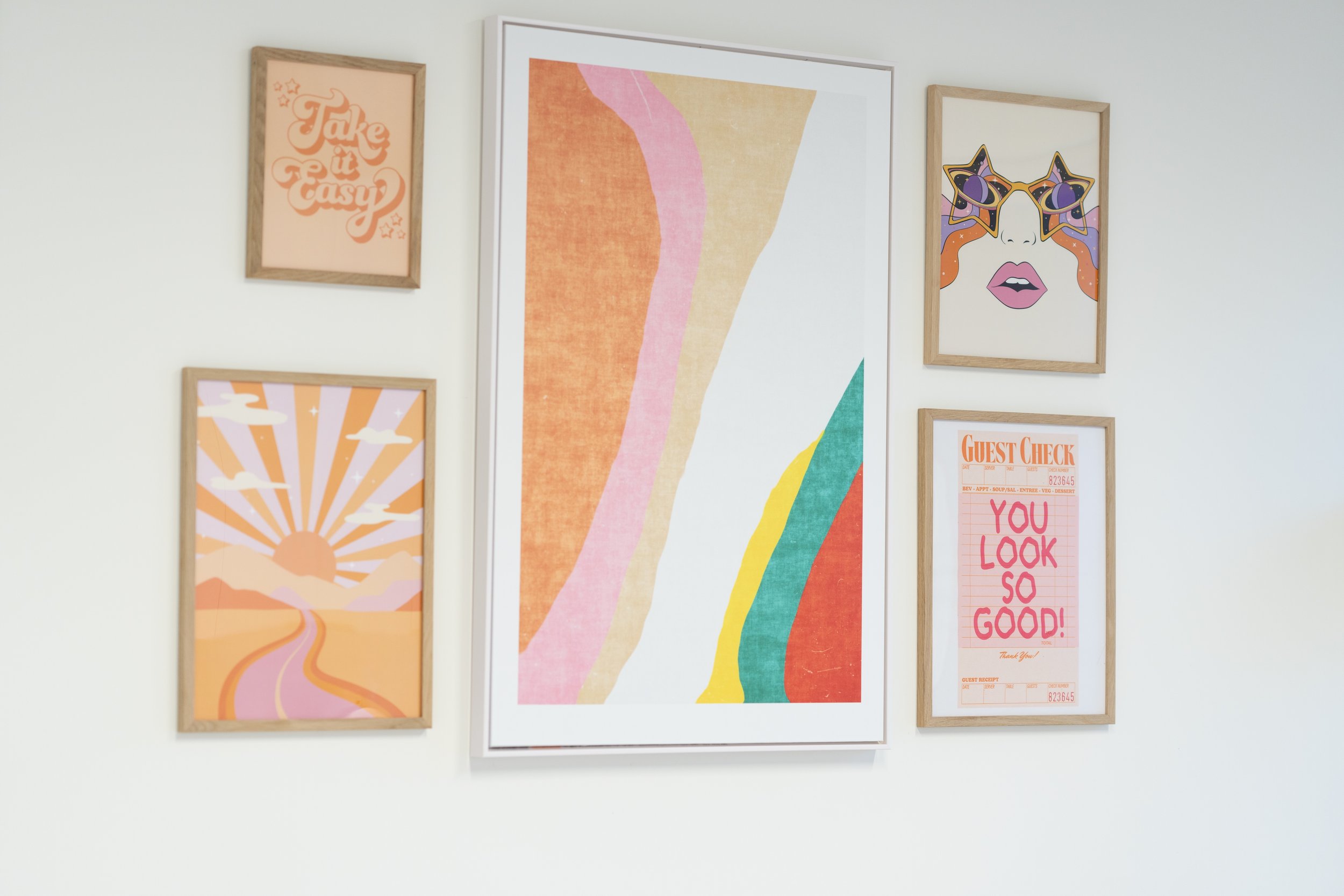 Collection of framed artwork displayed on a white wall inside the Ohara Dermatology office, featuring inspirational quotes, abstract designs, and colorful illustrations.