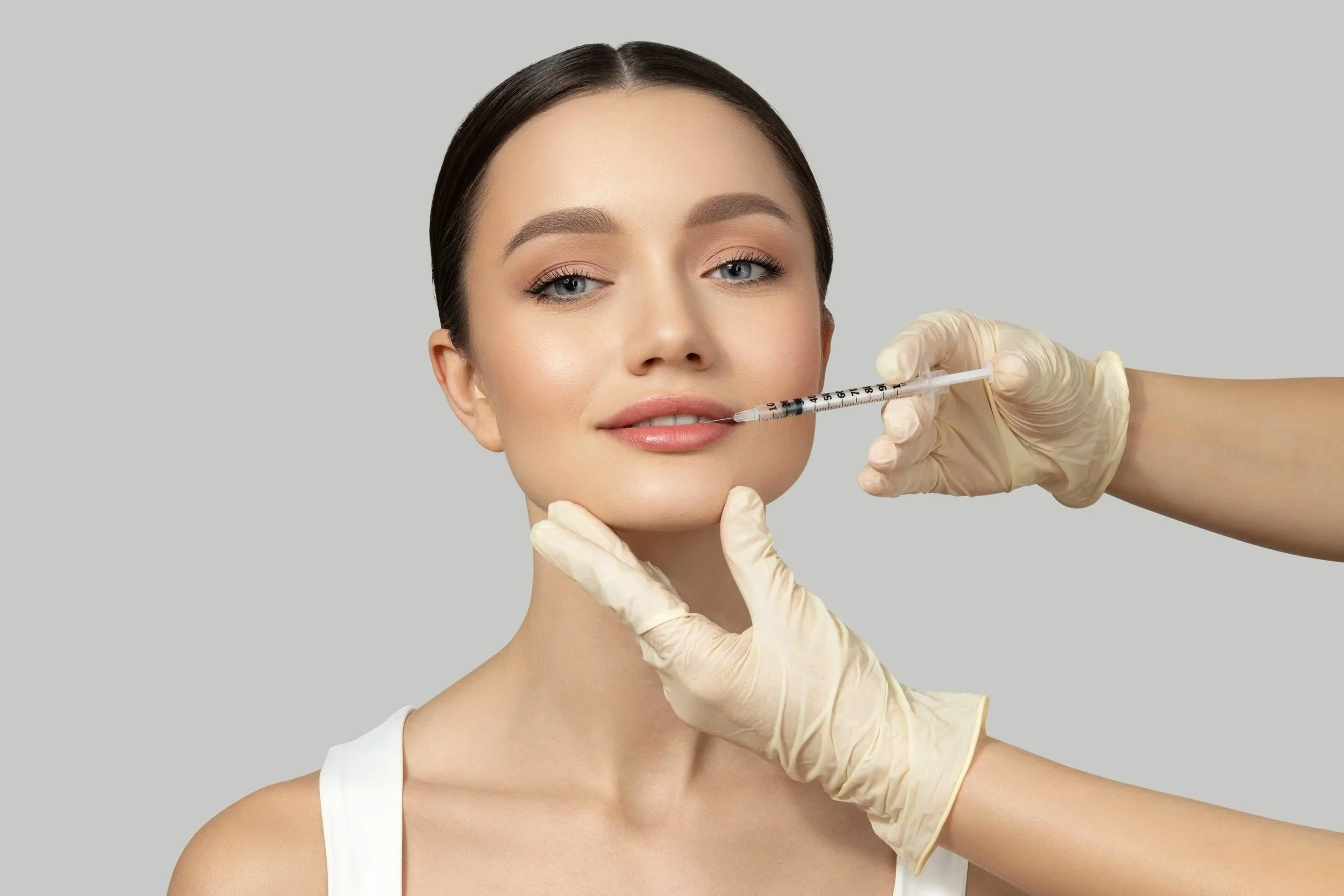 A woman receiving a cosmetic injection in her lips from a medical professional wearing gloves.