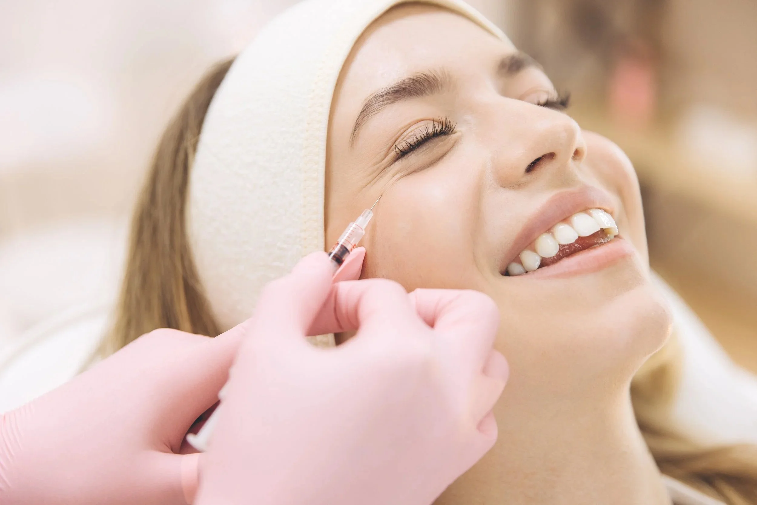 A woman smiling while receiving a cosmetic injection in her cheek.