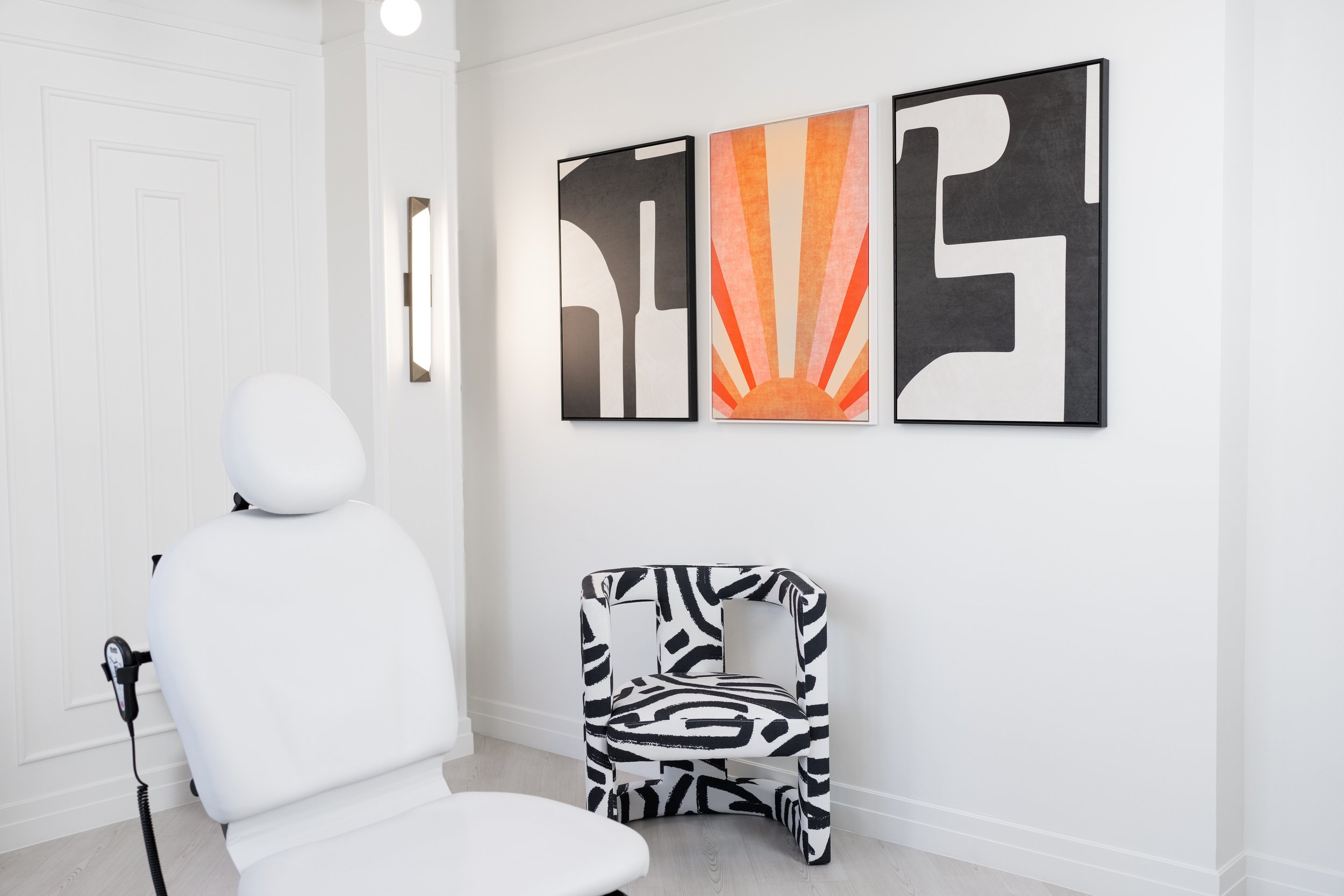 Minimalist examination room inside the Ohara Dermatology office featuring a white ergonomic chair, zebra-patterned chair, and framed abstract artwork on the wall.