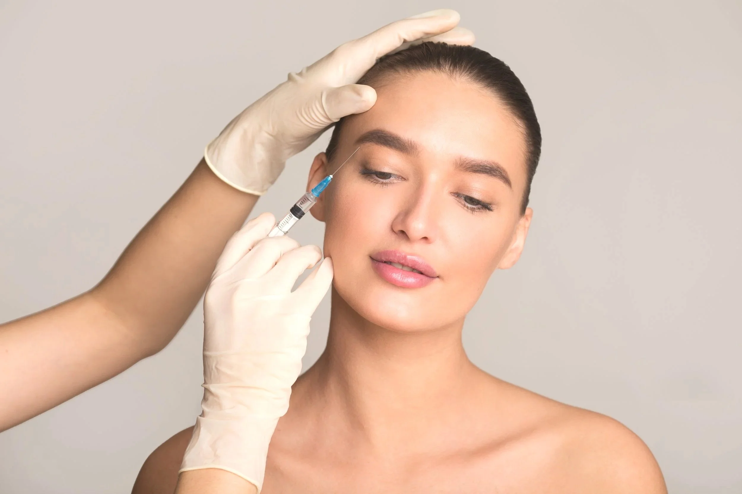 A woman receives a cosmetic injection in her cheek from a medical professional wearing gloves.