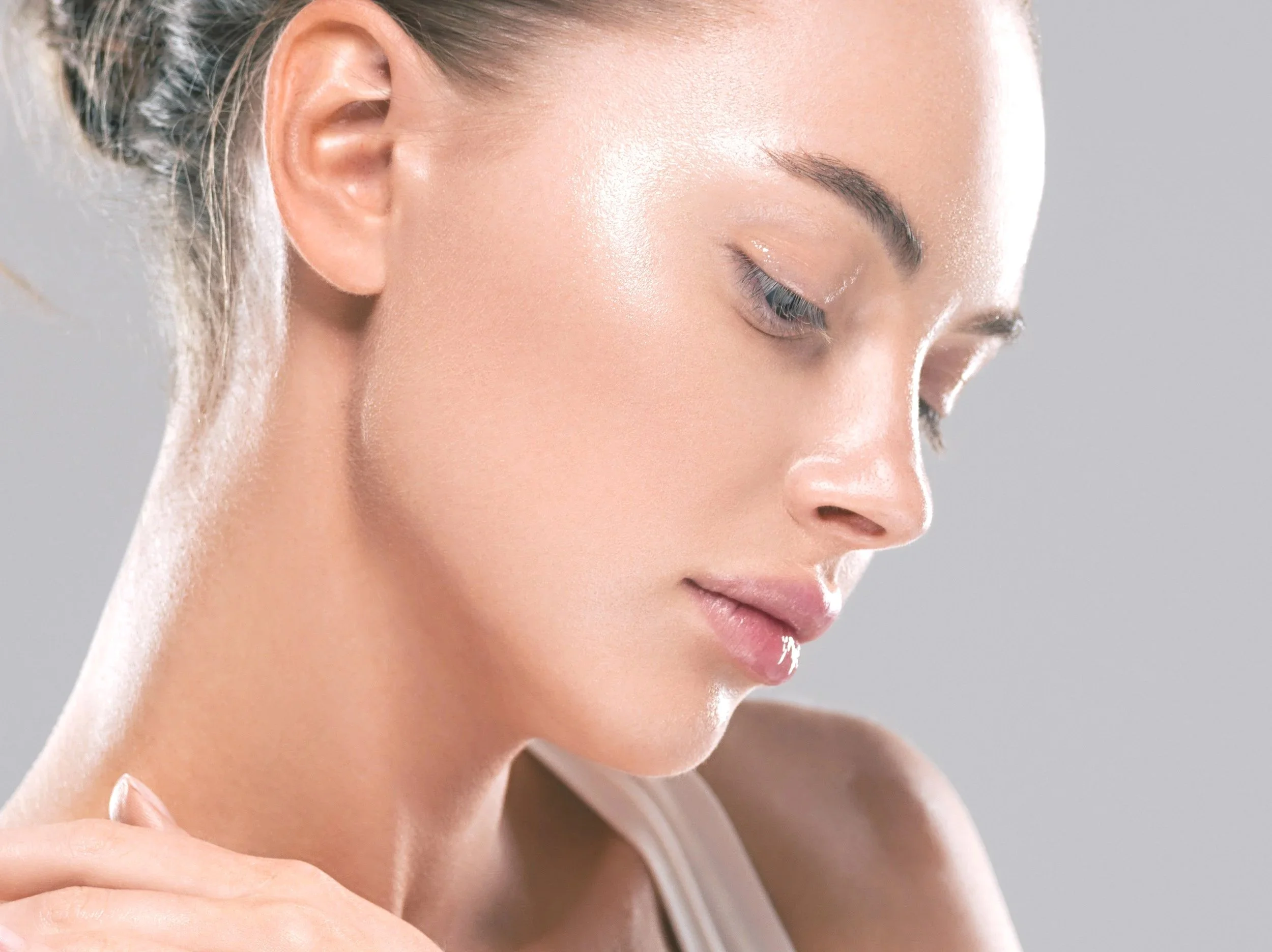 Close-up of a woman with clear, glowing skin and her eyes closed, with a soft gray background.
