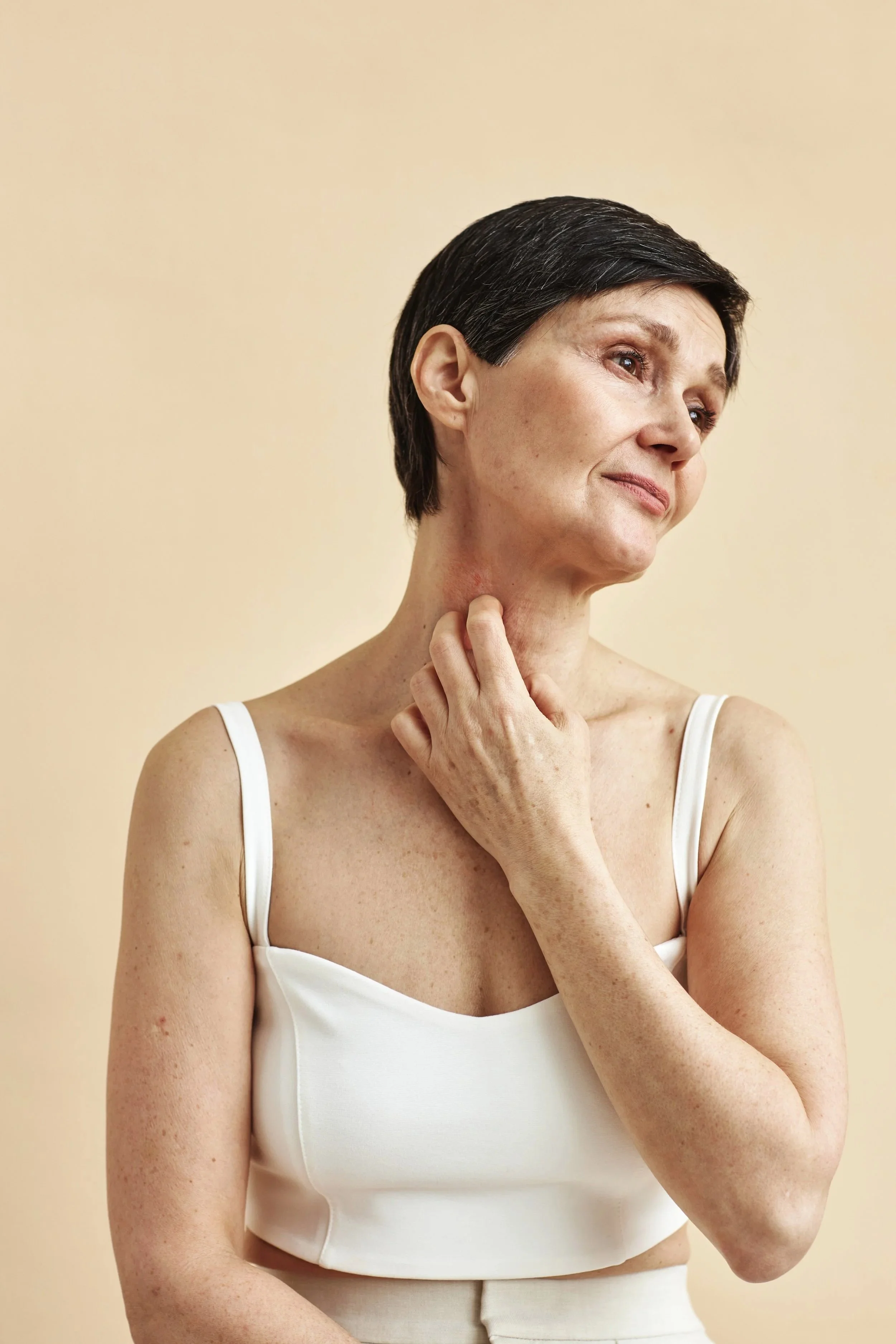 Woman touching her neck with visible skin concerns, representing psoriasis treatment and care in a dermatology setting.