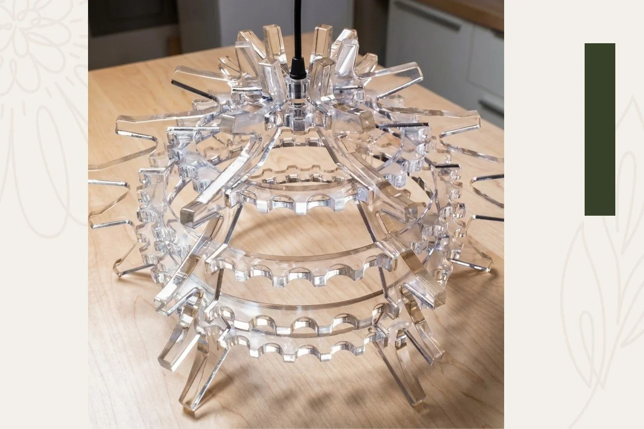 A clear, multi-tiered, spherical chandelier with gear-shaped rings and rods extending outward, sitting on a wooden surface.