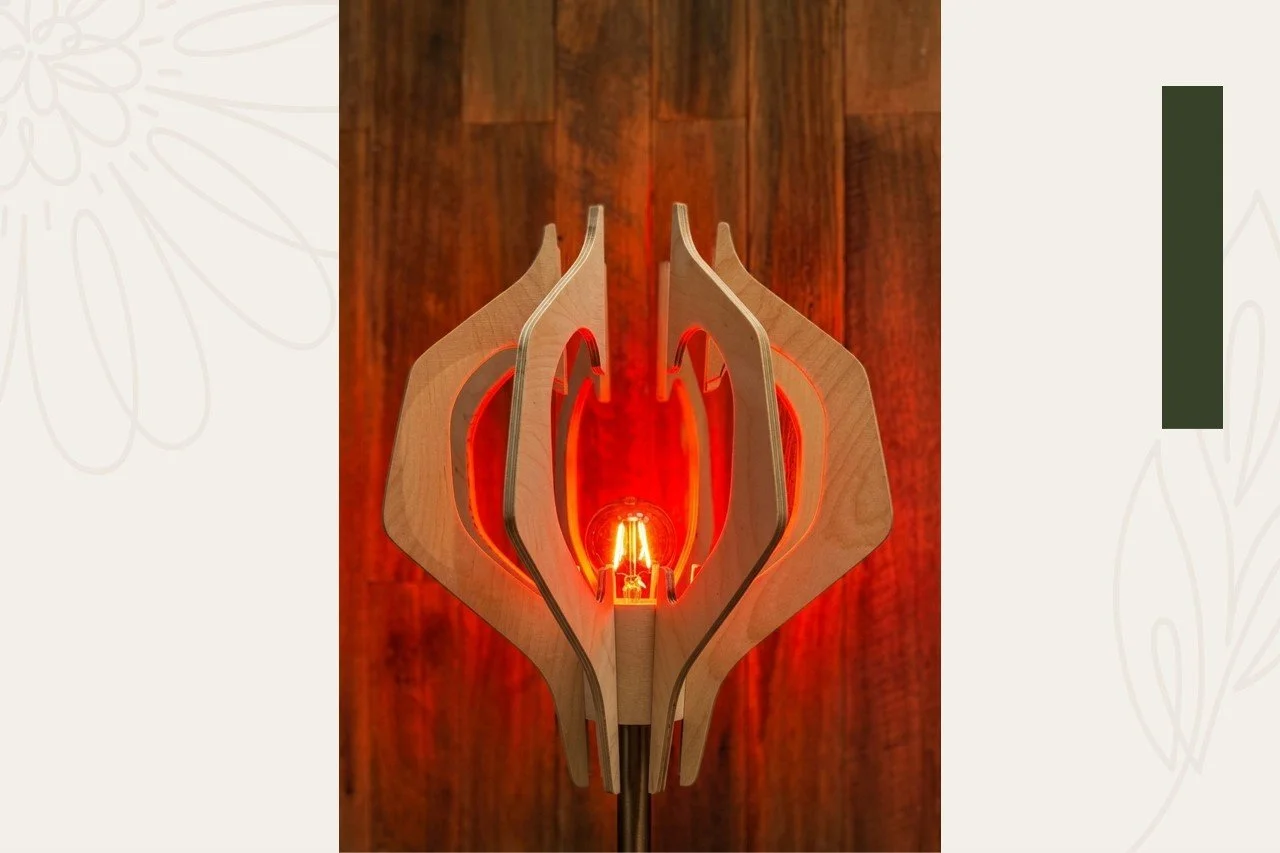 A modern wooden lamp with multiple layers and a visible filament light bulb inside, illuminated with a warm orange glow, set against a wooden background.
