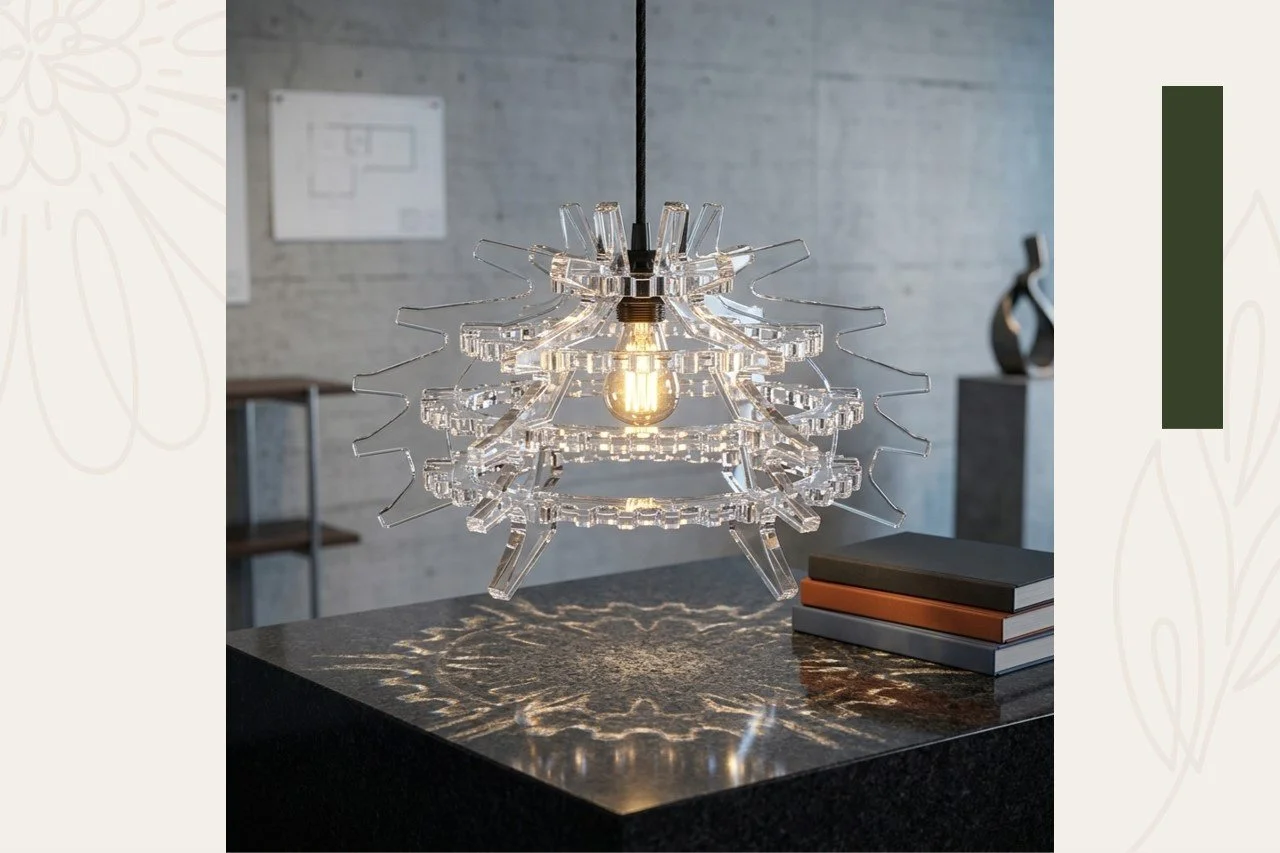 A modern pendant chandelier made of clear sculptural acrylic surrounding an exposed filament light bulb, hanging over a dark, polished countertop with books on it in a contemporary interior space.