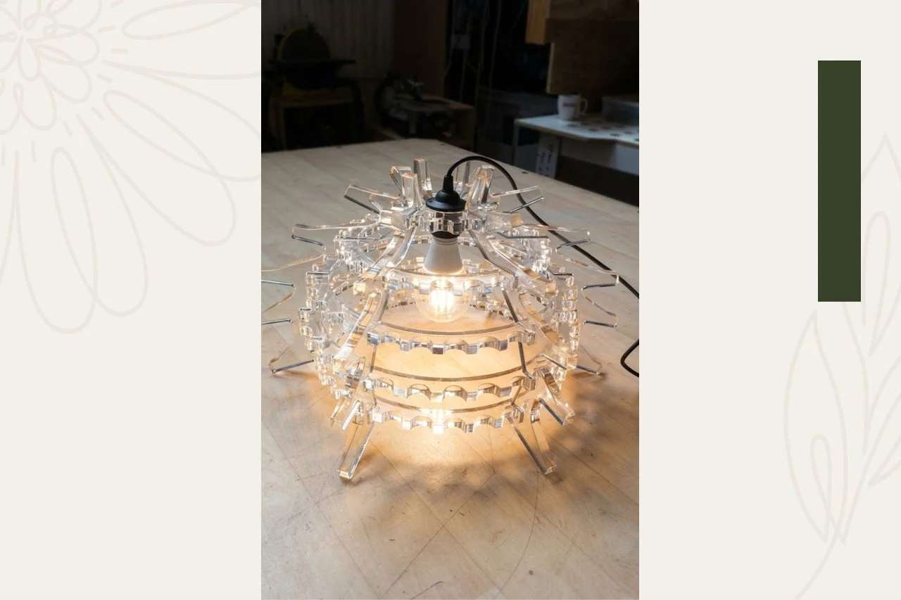 A decorative table lamp made of clear acrylic or plastic with multiple layered, curving horizontal ribs and a visible light bulb. It has a modern, artistic design and is placed on a wooden table.