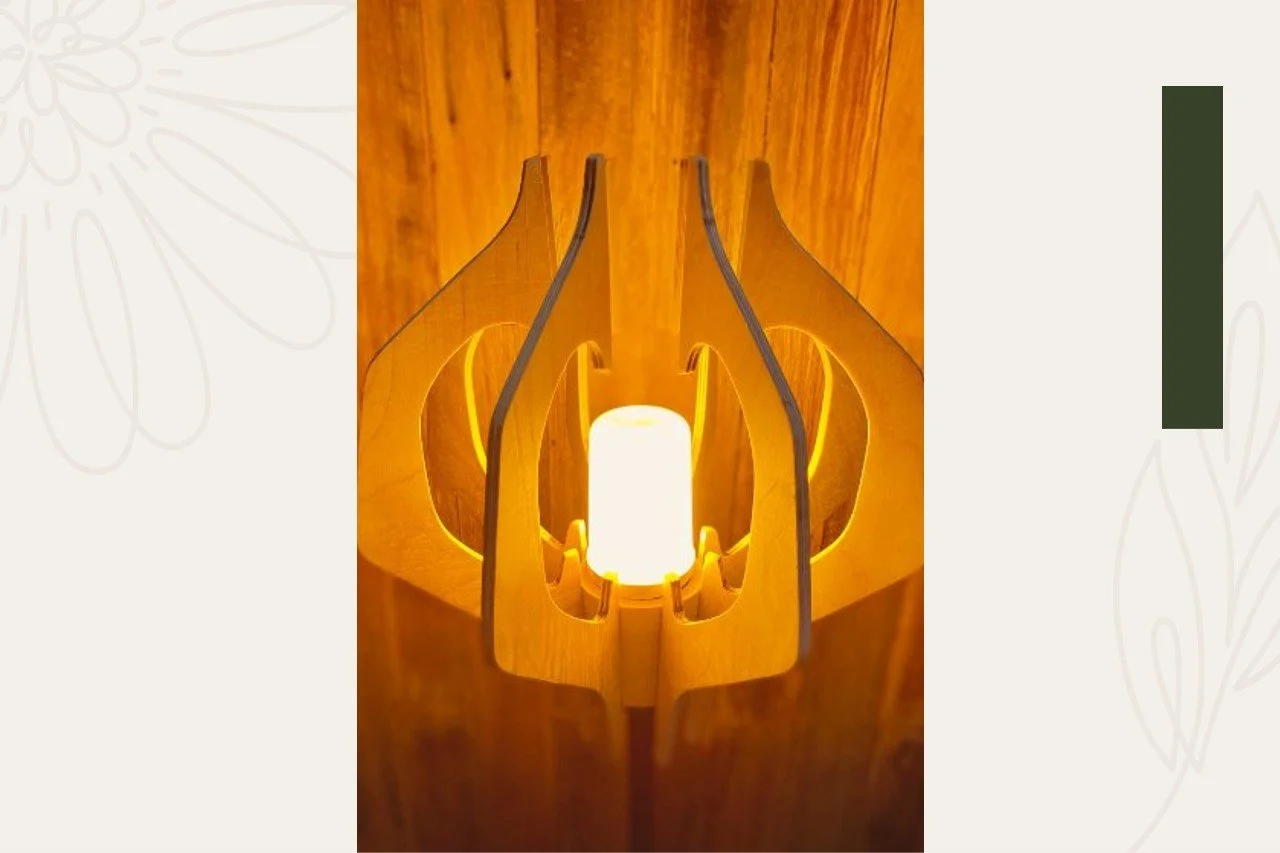 A modern table lamp with a cylindrical white shade, mounted inside a wooden structure with curved and cutout design, emitting warm light.