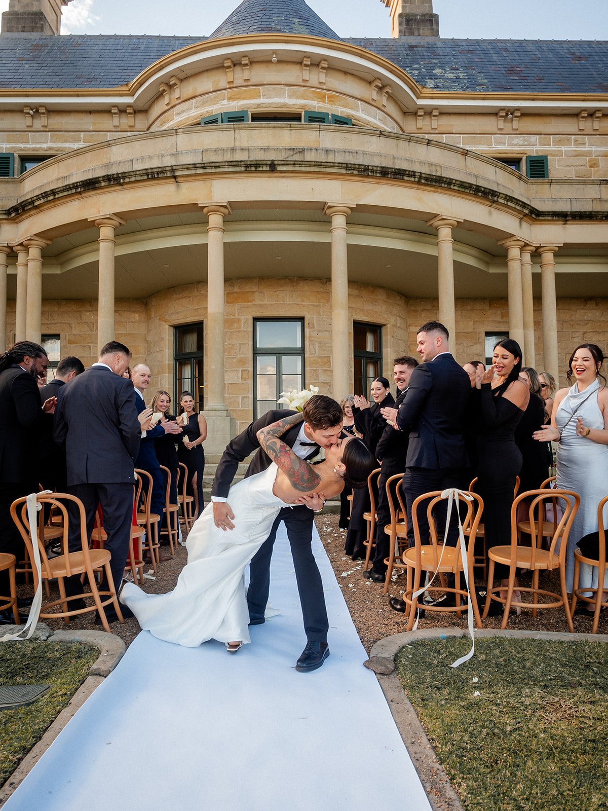 Cherry and Nick dip kiss while exiting down the aisle at Jimbour House with cheering guests — Sean Reefman Photography