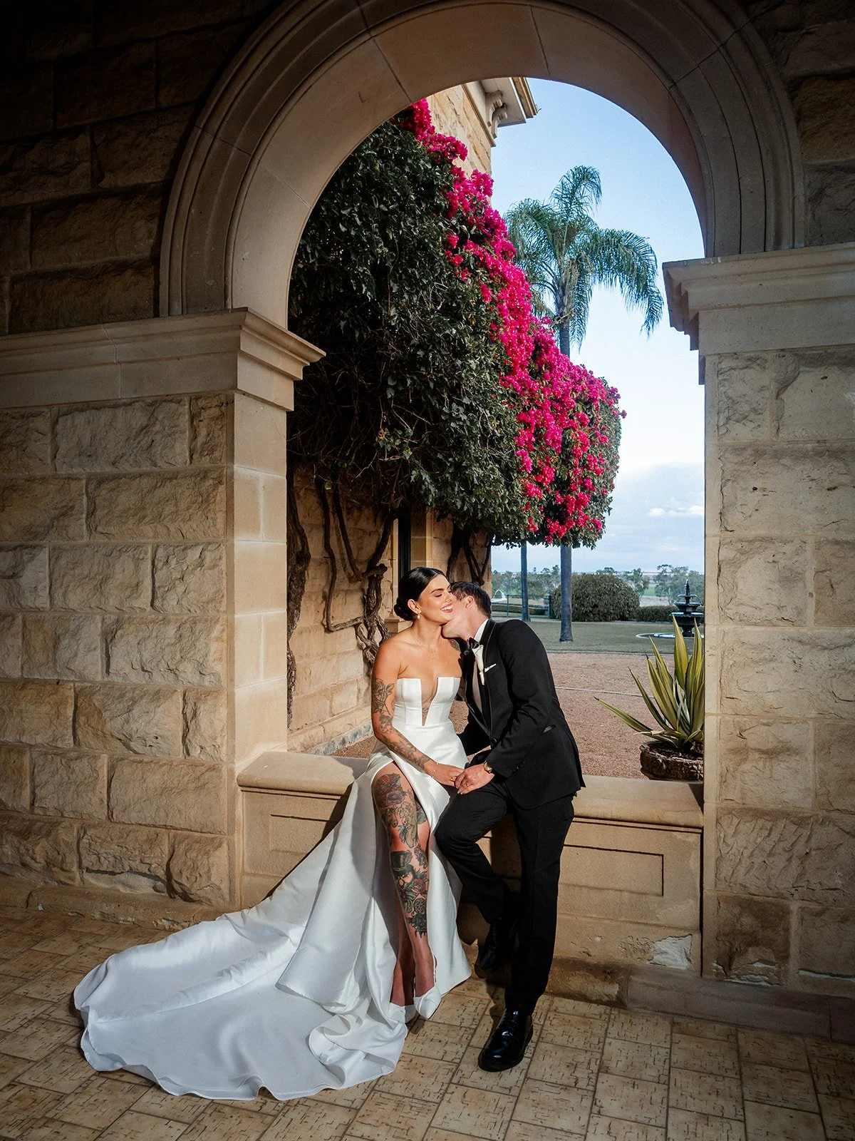 Cherry and Nick kissing in the sandstone archway at Jimbour House with bougainvillea — Darling Downs wedding by Sean Reefman Photography