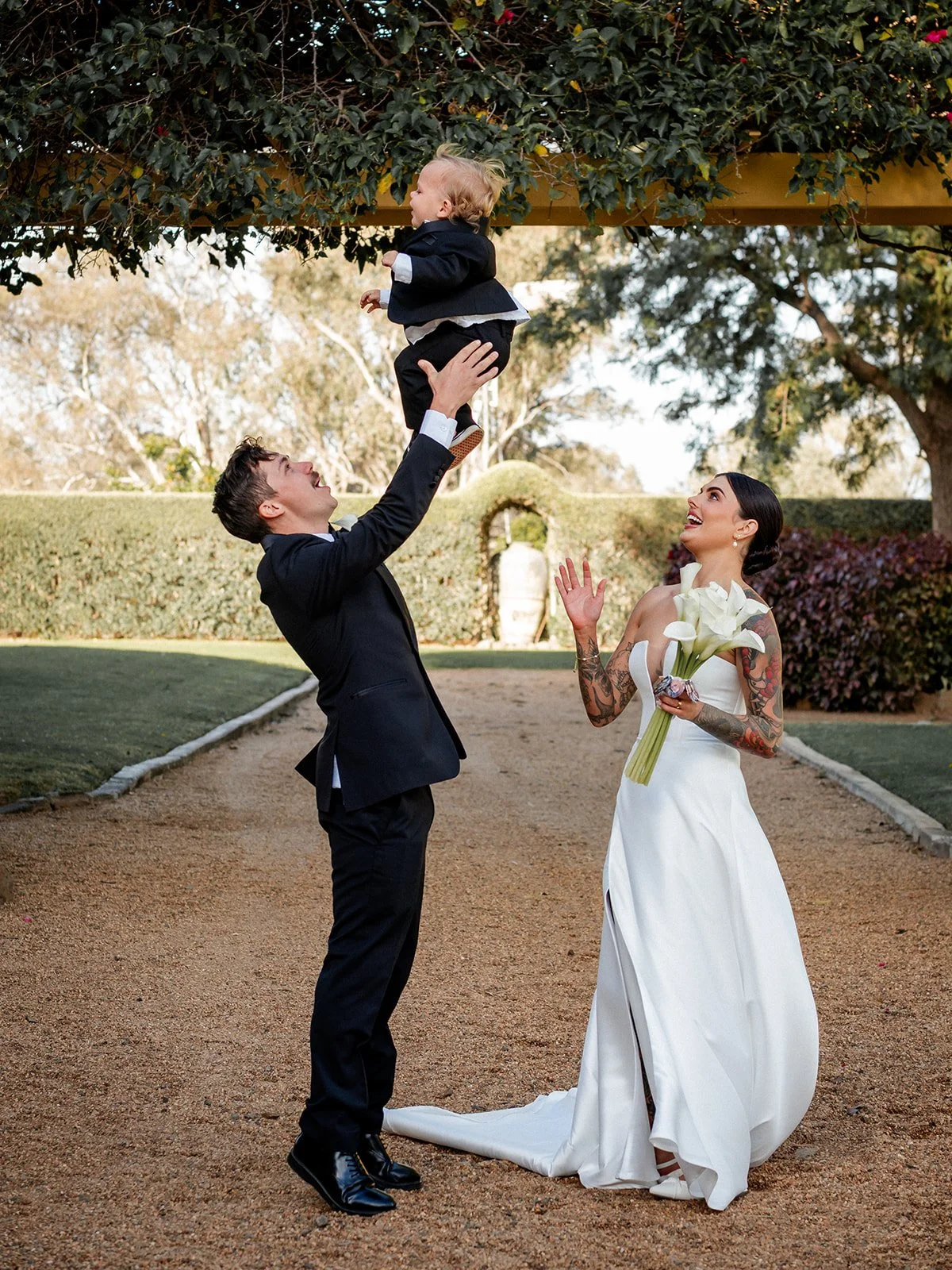 Nick lifting baby in the air laughing while Cherry looks on in Jimbour House gardens — Sean Reefman Photography