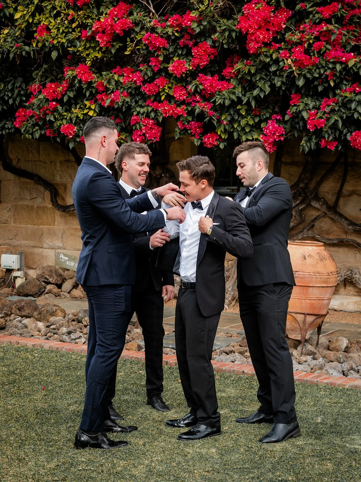 Groomsmen helping Nick get ready outside Jimbour House with bougainvillea backdrop — Sean Reefman Photography