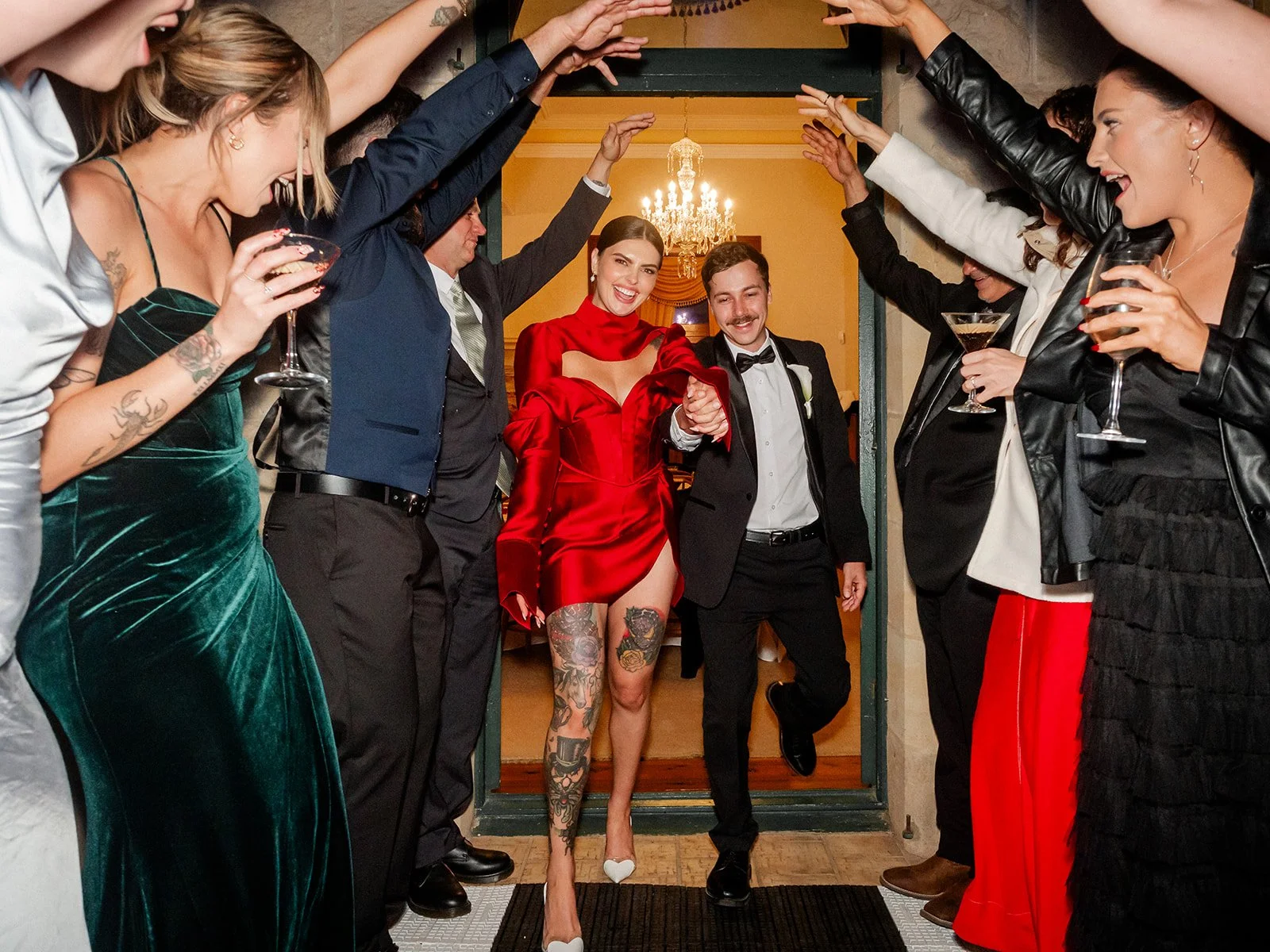 Cherry in red Khirzad Femme reception dress entering through archway with Nick and cheering guests — Jimbour House wedding by Sean Reefman Photography