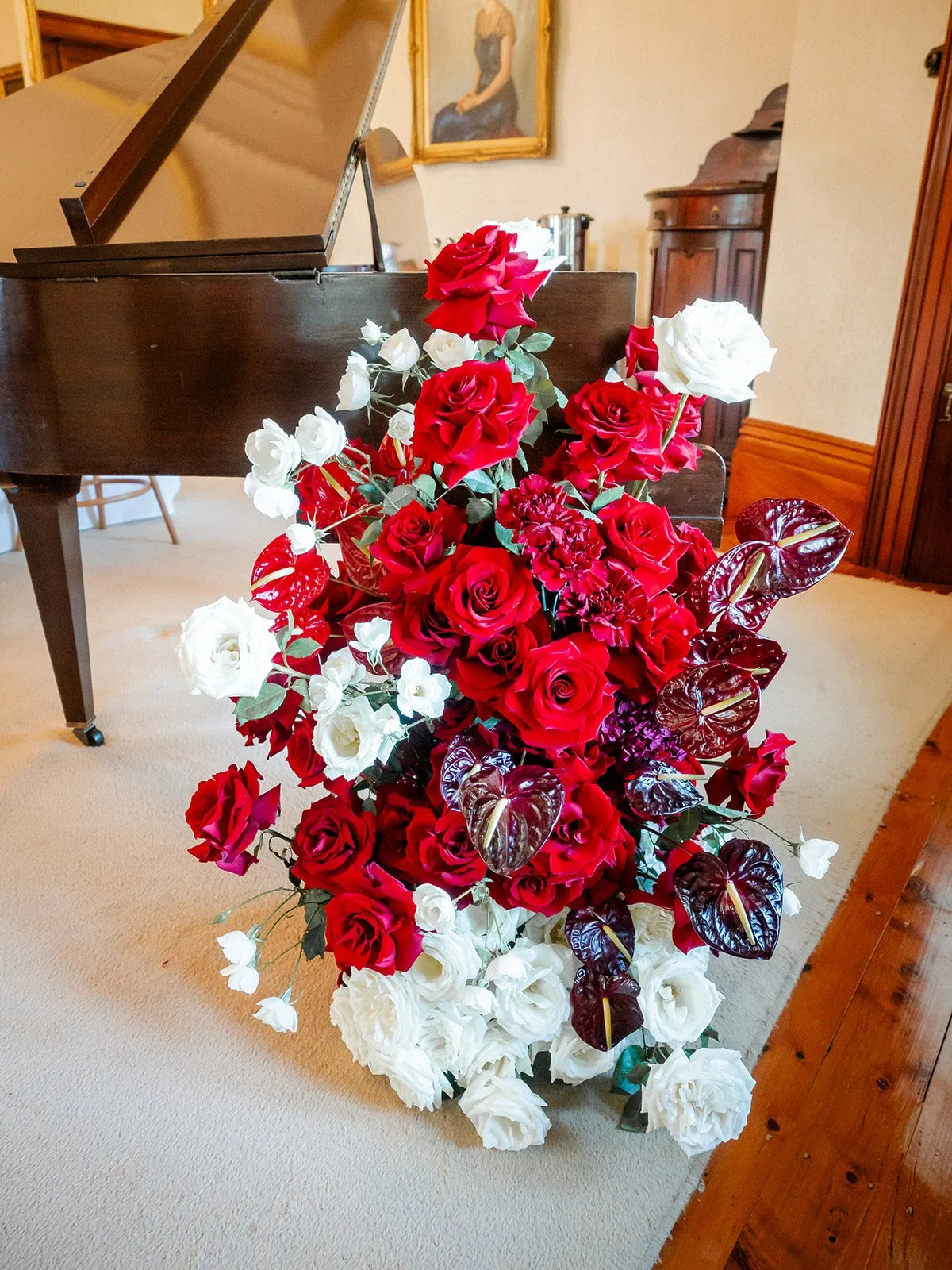 Large red and white rose floral arrangement beside grand piano inside Jimbour House reception room — Sean Reefman Photography
