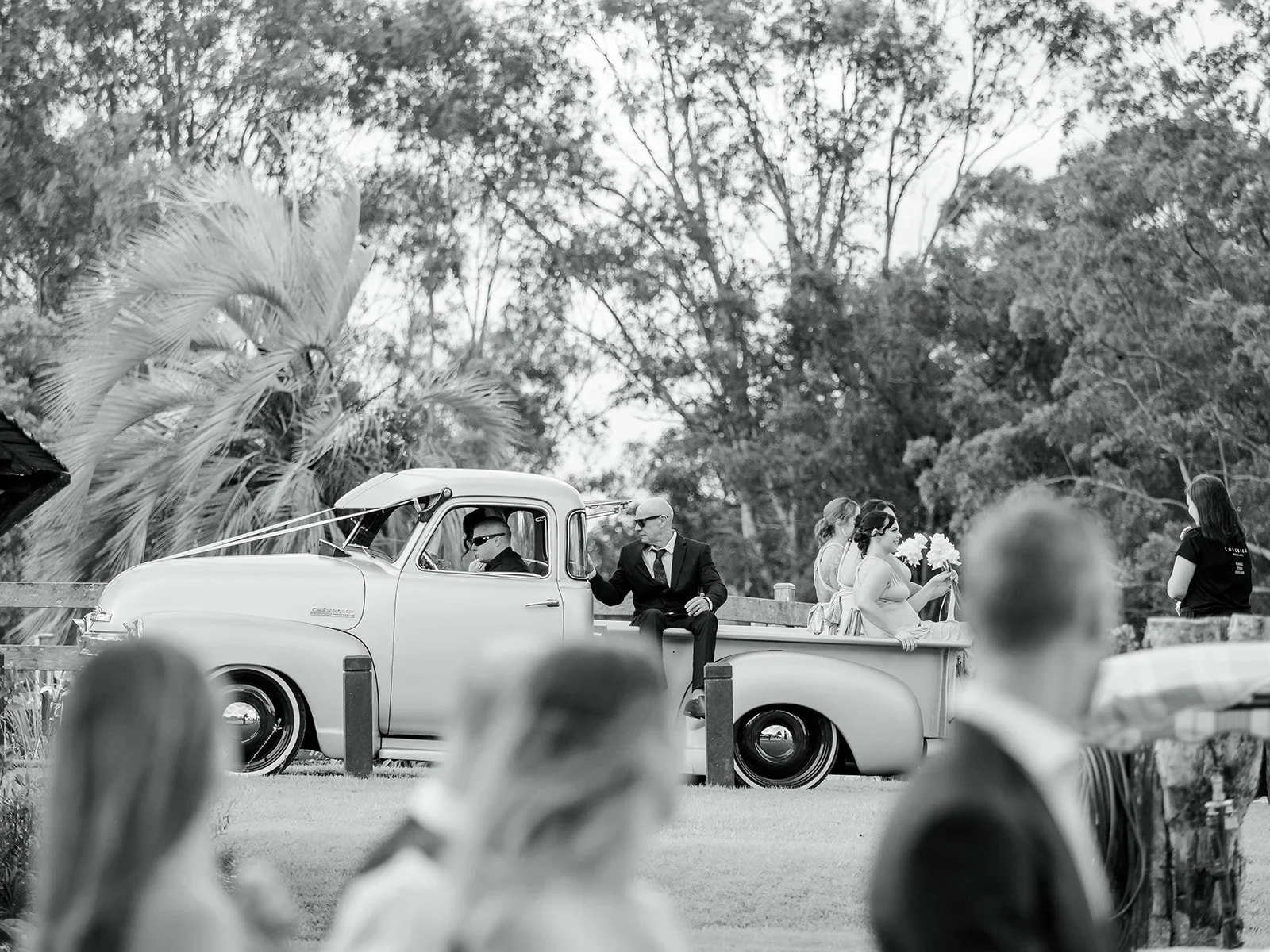 Guests gathering as the bride arrives by vintage car in black and white — Sean Reefman Photography