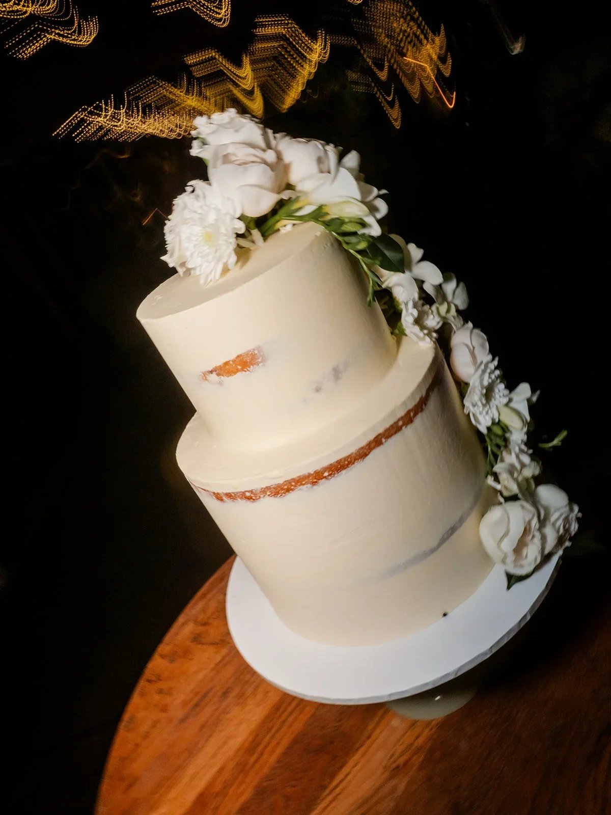 Three-tier wedding cake styled with white florals and gold leaf detail — Sean Reefman Photography