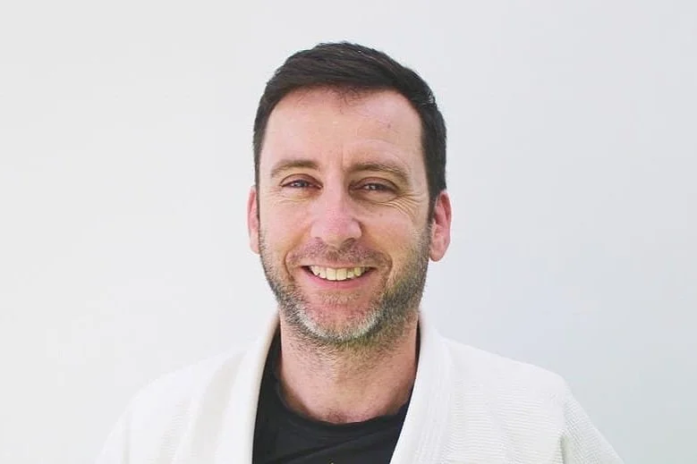 Trent is a male wearing a white gi and a black rashguard.  He is smiling.