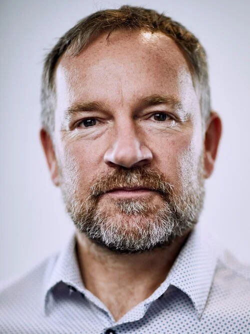 Portrait of a bearded man with short hair and a white patterned shirt