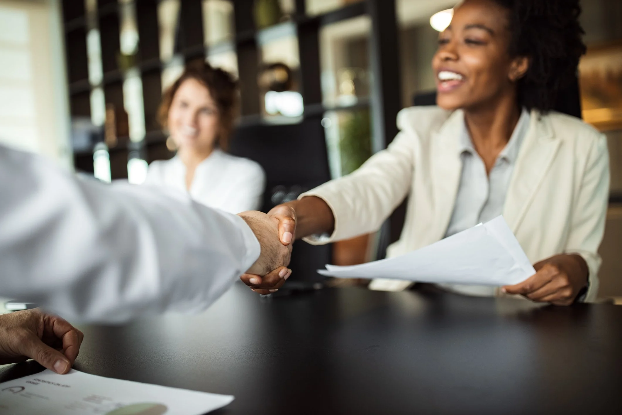 An office work holds a contract and shakes hands with a prospective new employer.