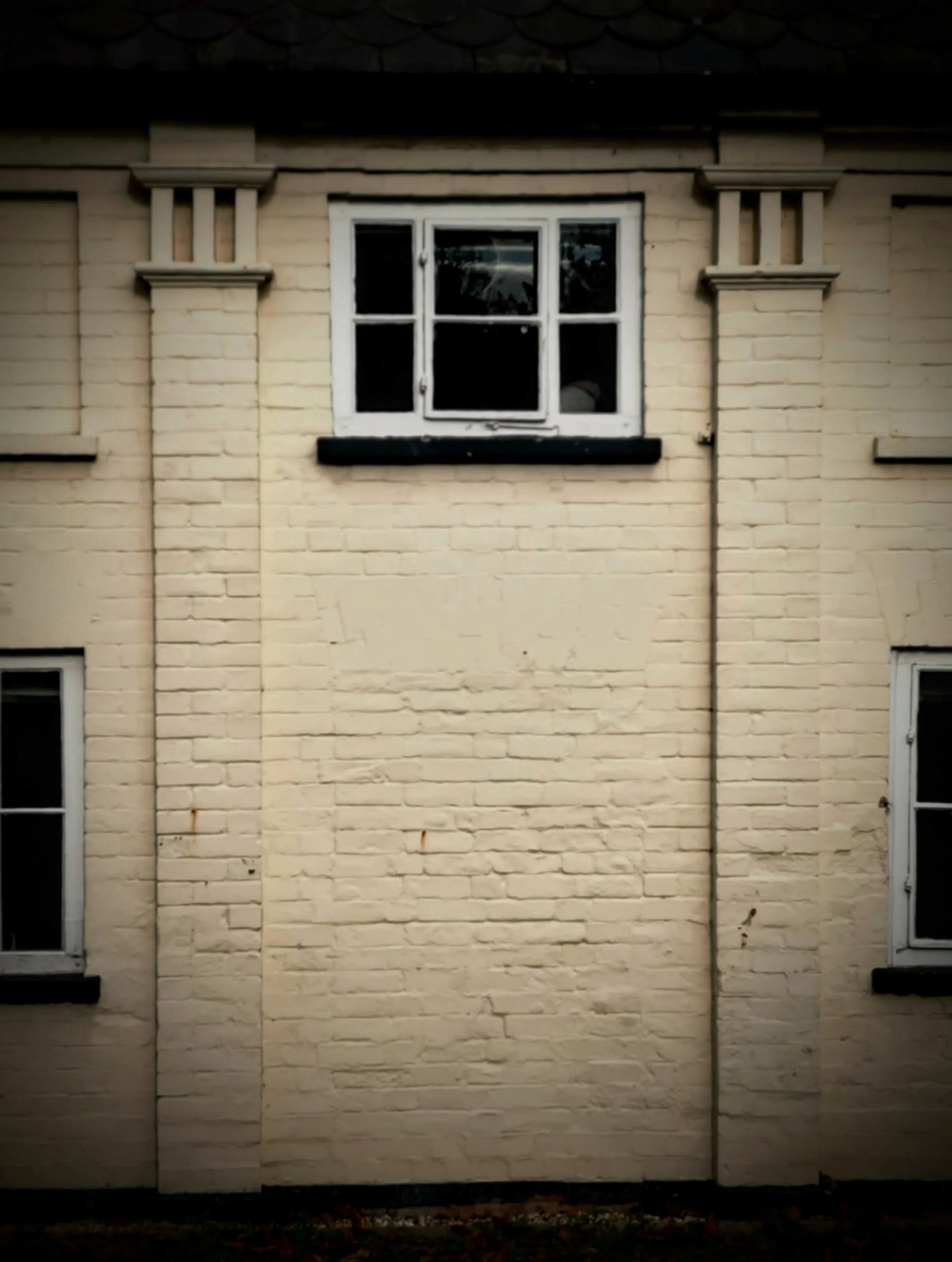 Exterior of a painted brick building with three windows, featuring a large window above and smaller windows on each side, all with white frames and black sills.