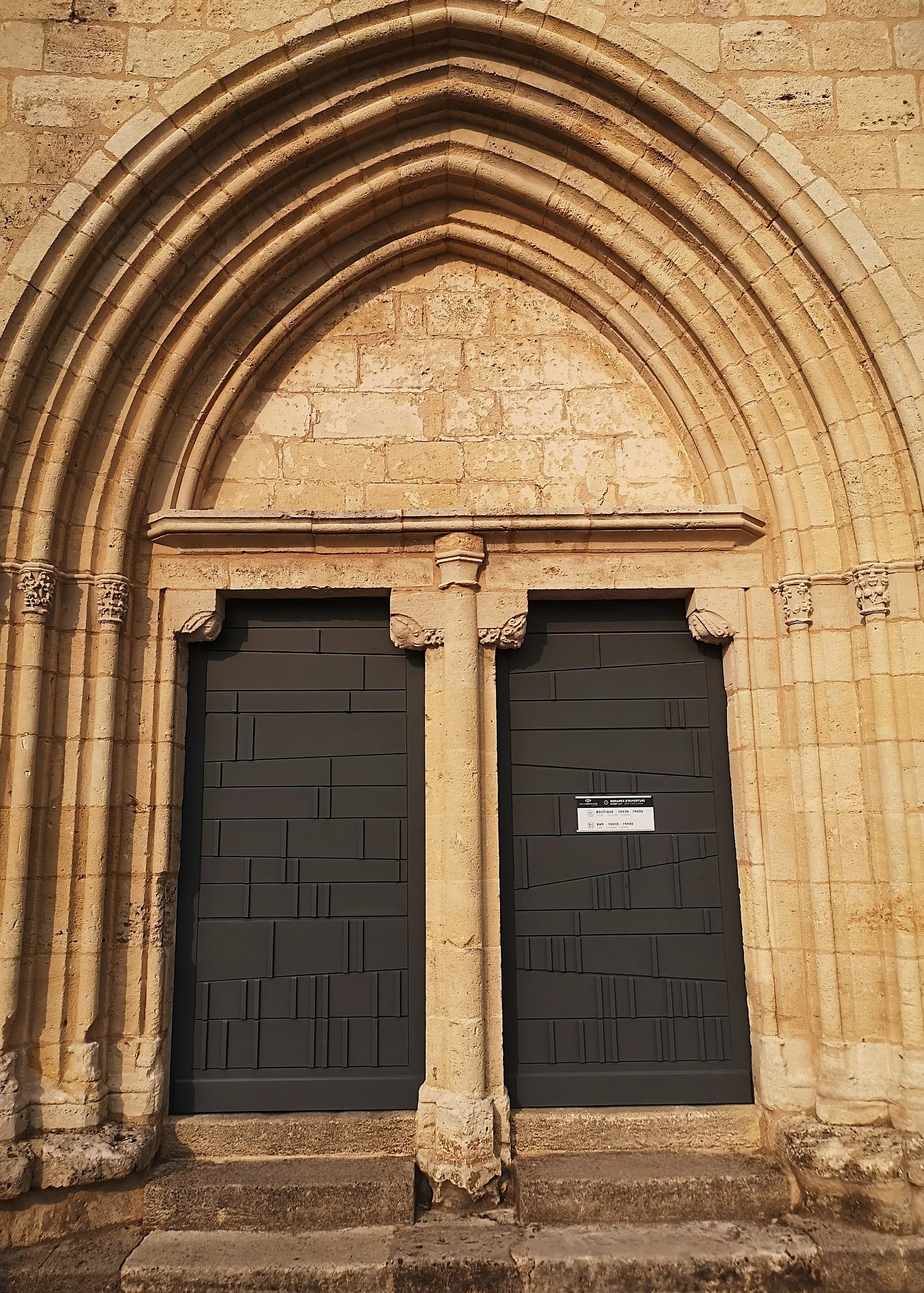 Close-up of a stone church entrance with two black modern doors set into a Gothic-style pointed archway.