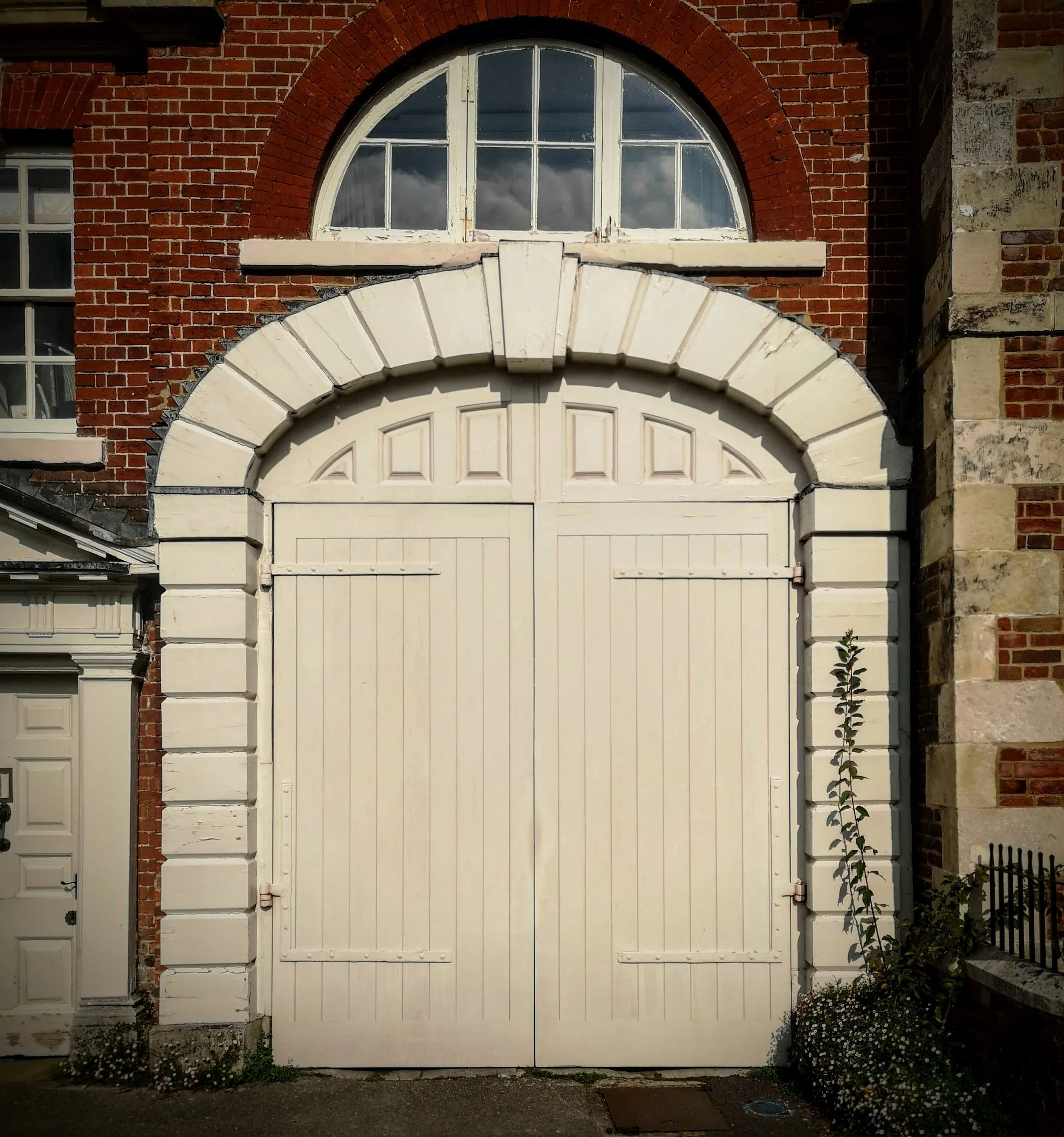 White double door entrance with arched window above, framed by red brick and stone walls.