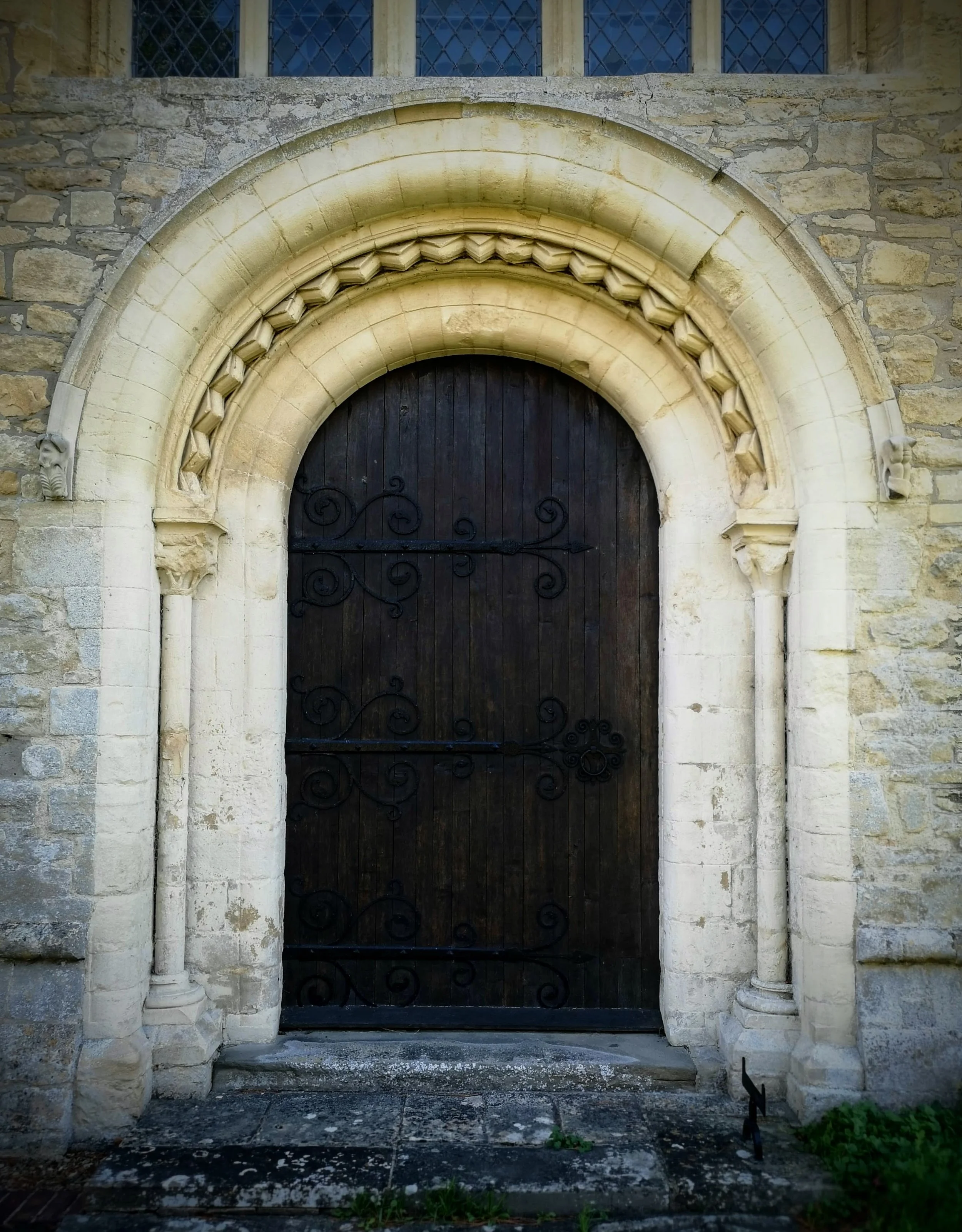 A large wooden church door framed by an ornate stone archway with decorative carvings, set in a stone wall.