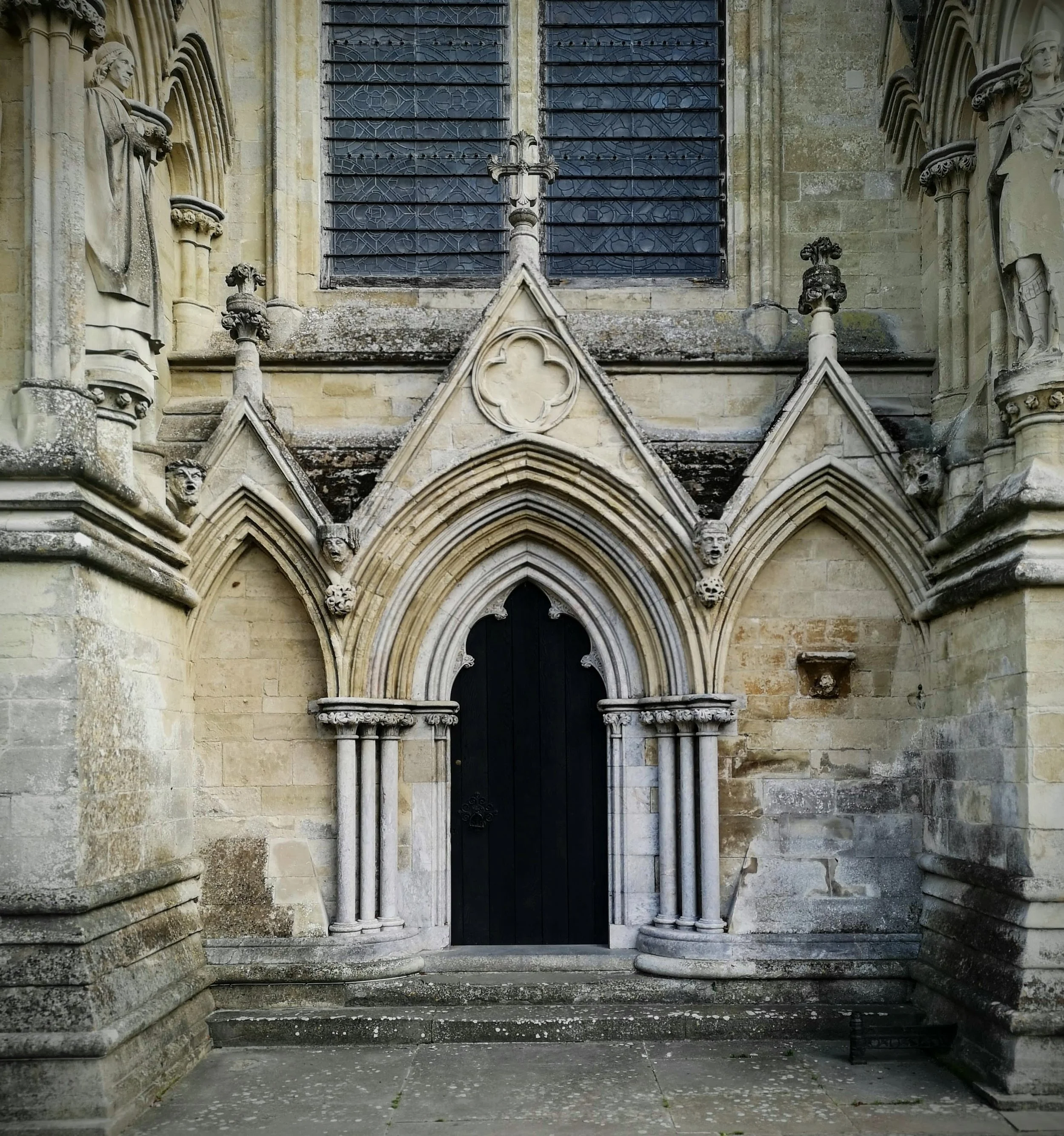The entrance of a historic Gothic church with pointed arches, columns, and ornate stone carvings, including devil and human faces, on the facade.