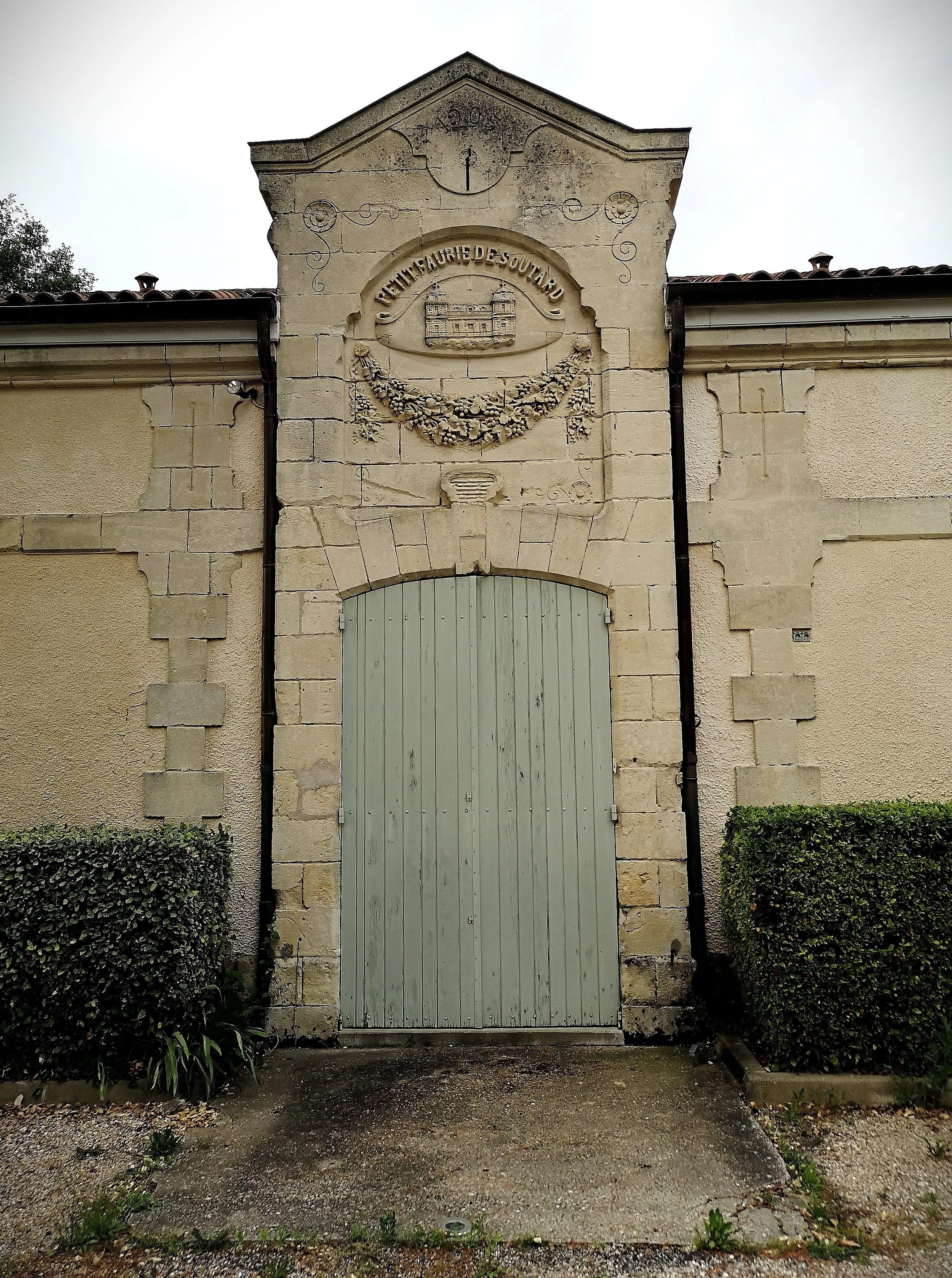 A beige stone and stucco building with an arched wooden door, topped with an ornate stone crest featuring a castle, floral garland, and the inscription "CHATEAU DE VAUBURNAU."