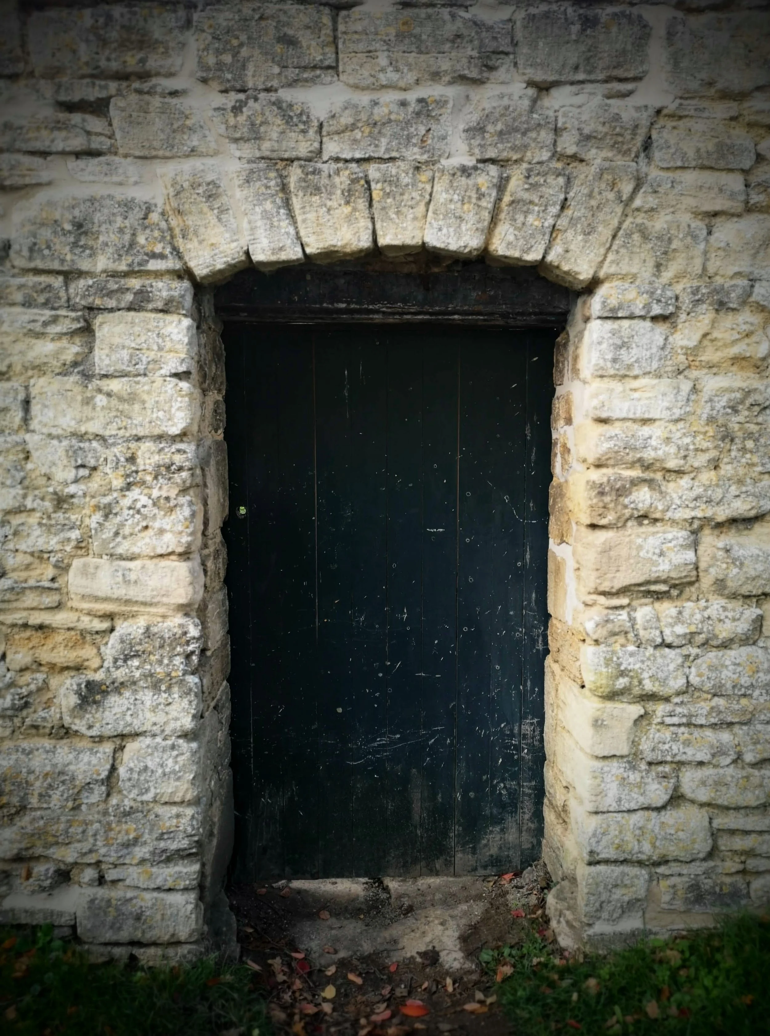 A black wooden door set into a stone wall with a stone arch above it.