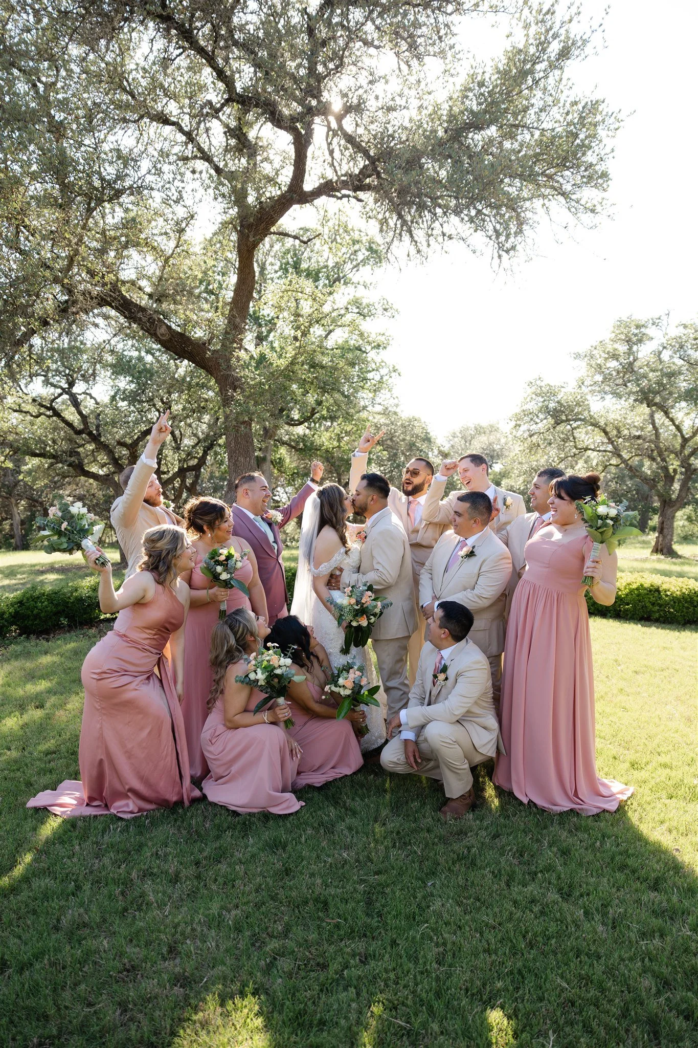 A person holding a large bouquet of red, pink, white, and green flowers while hugging another person at an indoor event with a blurred group of people in the background.