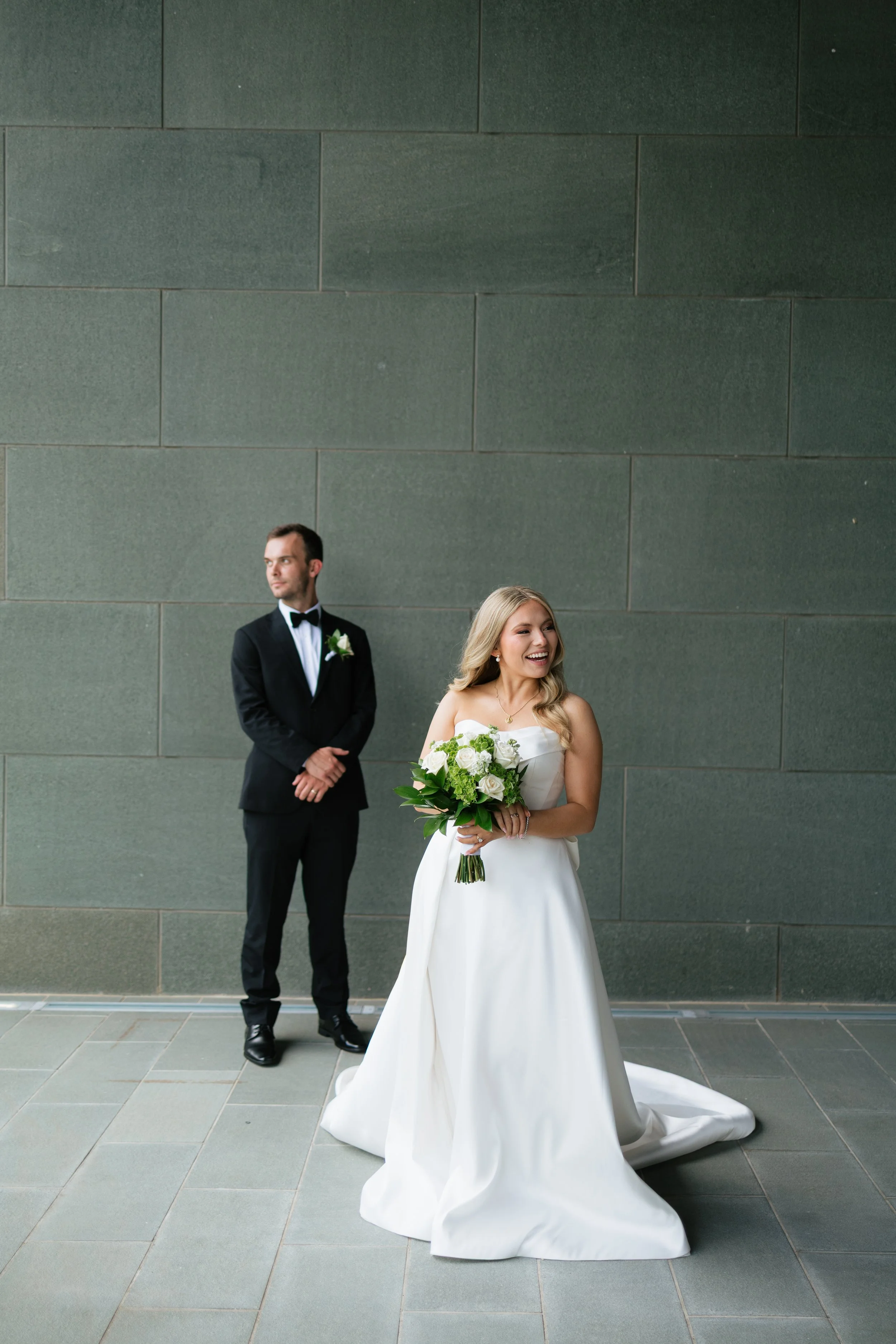 A bride and three bridesmaids standing together in a rustic archway, holding bouquets of orange, yellow, and deep red flowers, dressed in warm-toned dresses.