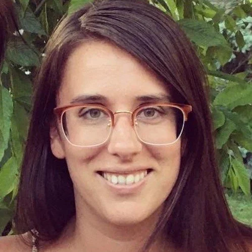 Woman with long brown hair and glasses smiling outdoors