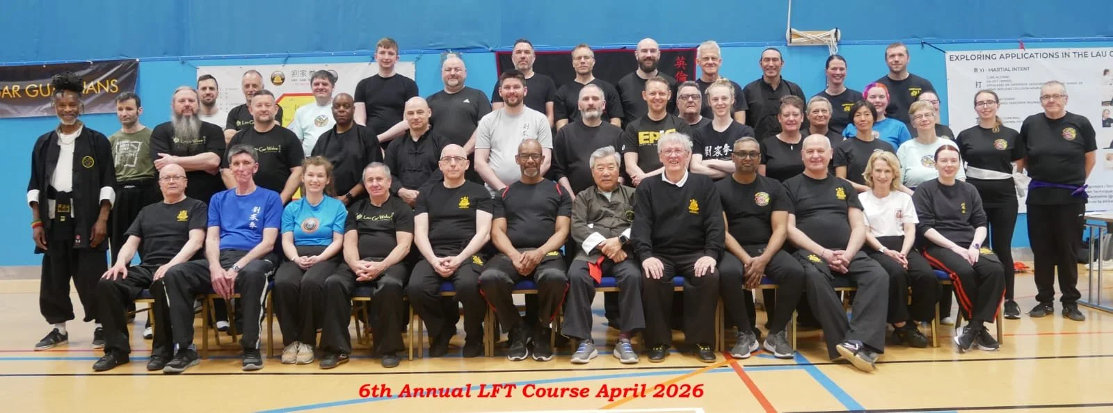 Group photo of martial artists at the 6th Annual LFT Course in April 2026, posing in a gymnasium with banners and posters on the walls.