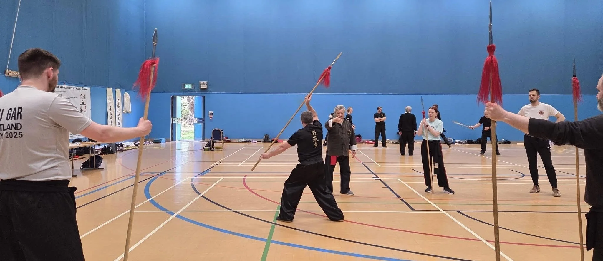 People practicing martial arts with spears in a gym.