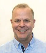 Smiling man with short blond hair, wearing a light blue collared shirt.