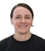 Portrait of a woman with dark hair wearing a black top, smiling, against a white background.