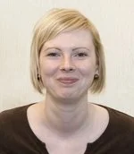 A woman with short blonde hair smiling against a plain background.