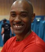 Smiling man in red athletic shirt at indoor sports event, with blue curtains in the background.