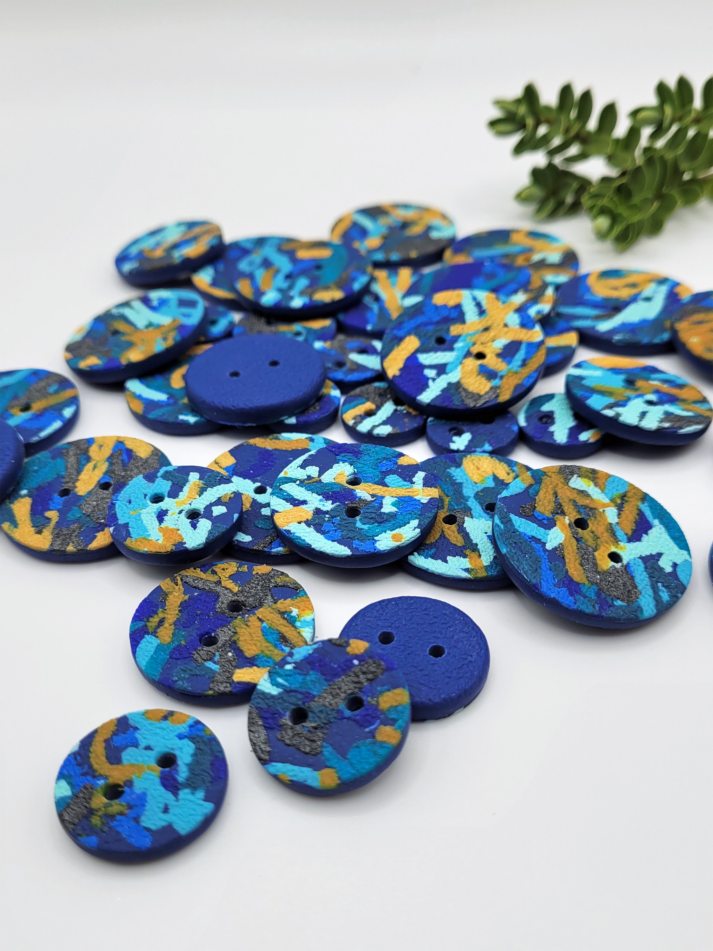 A pile of blue, grey and orange Ticker Tape Buttons, each with a unique surface pattern and colour mix.