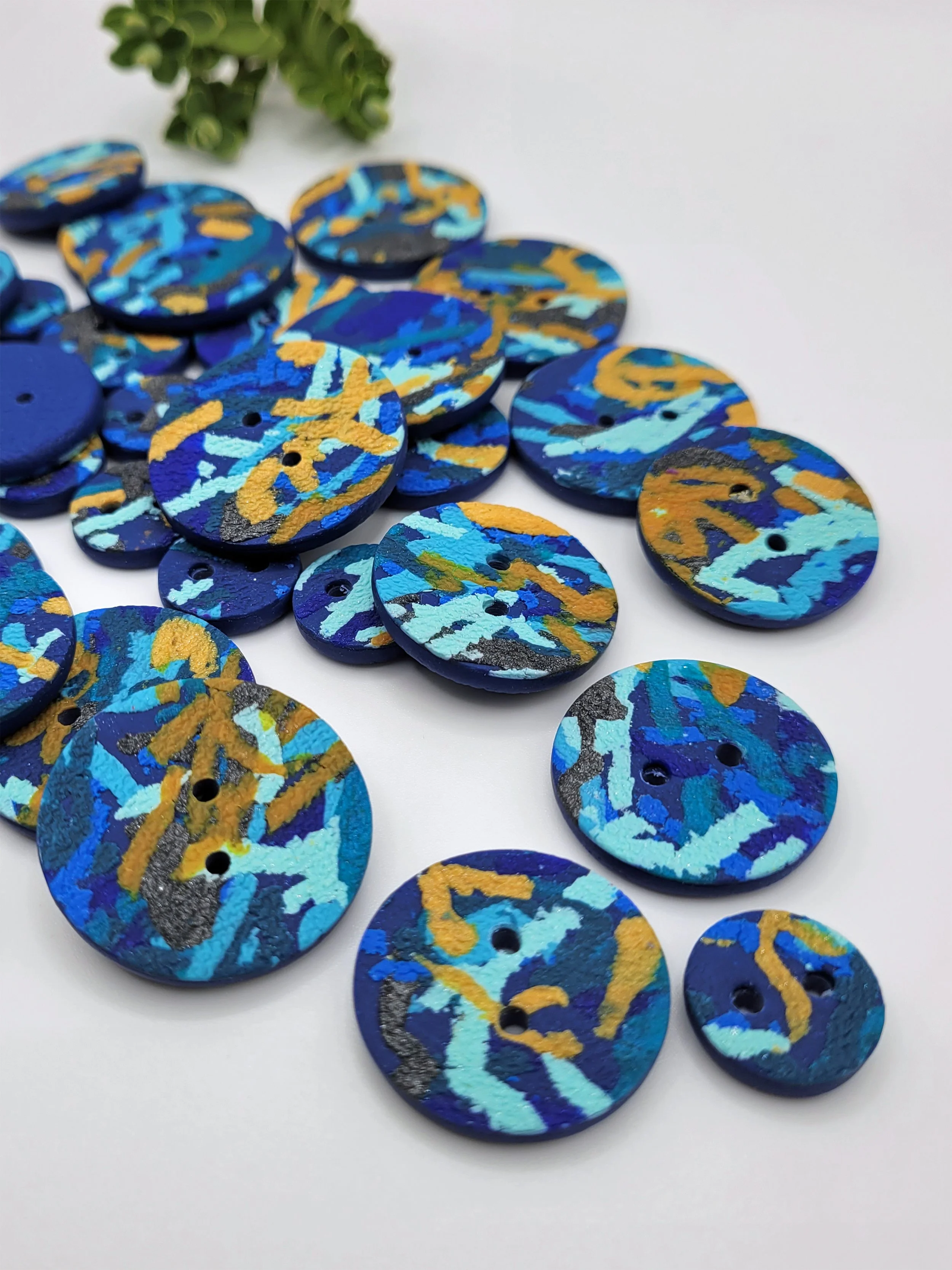 Mixed sizes of Blue Ticker Tape buttons, some with their navy blue backs showing.