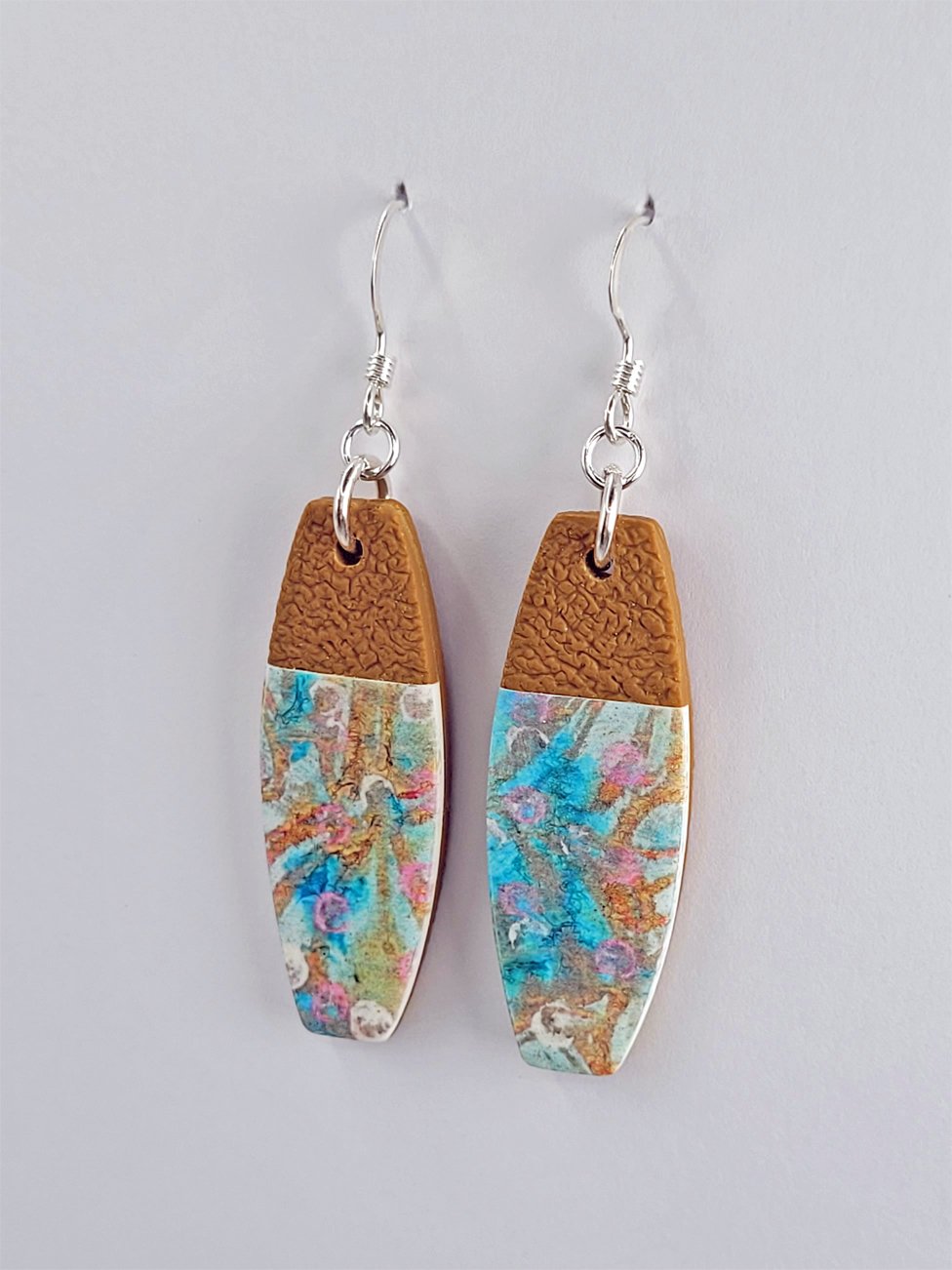 Close-up of tablet earrings showing their smooth floral front and textured ginger polymer clay tops and backs for contrast.