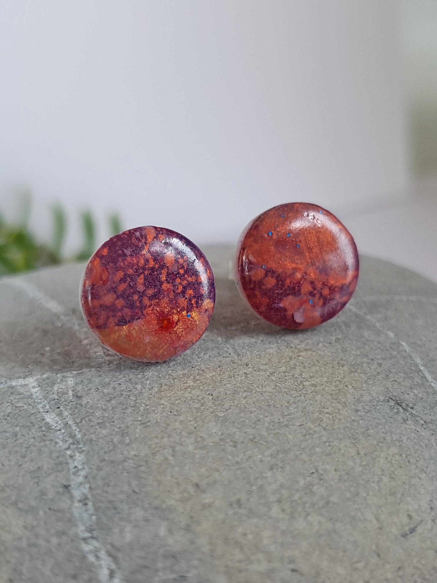 Left side of lightweight polymer clay stud earrings with a hand painted splatter pattern in brown, purple, gold, and bronze with a gloss shine.