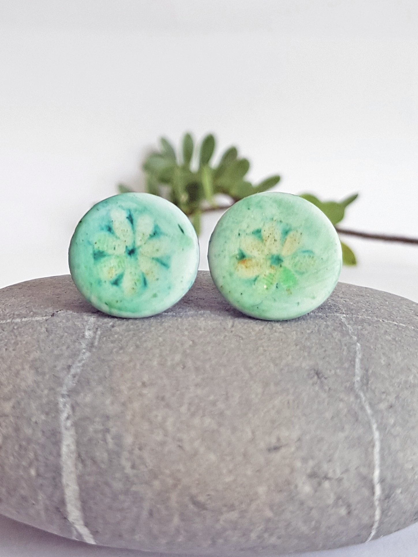 Front of turquoise polymer clay stud earring with distressed flower motif.
