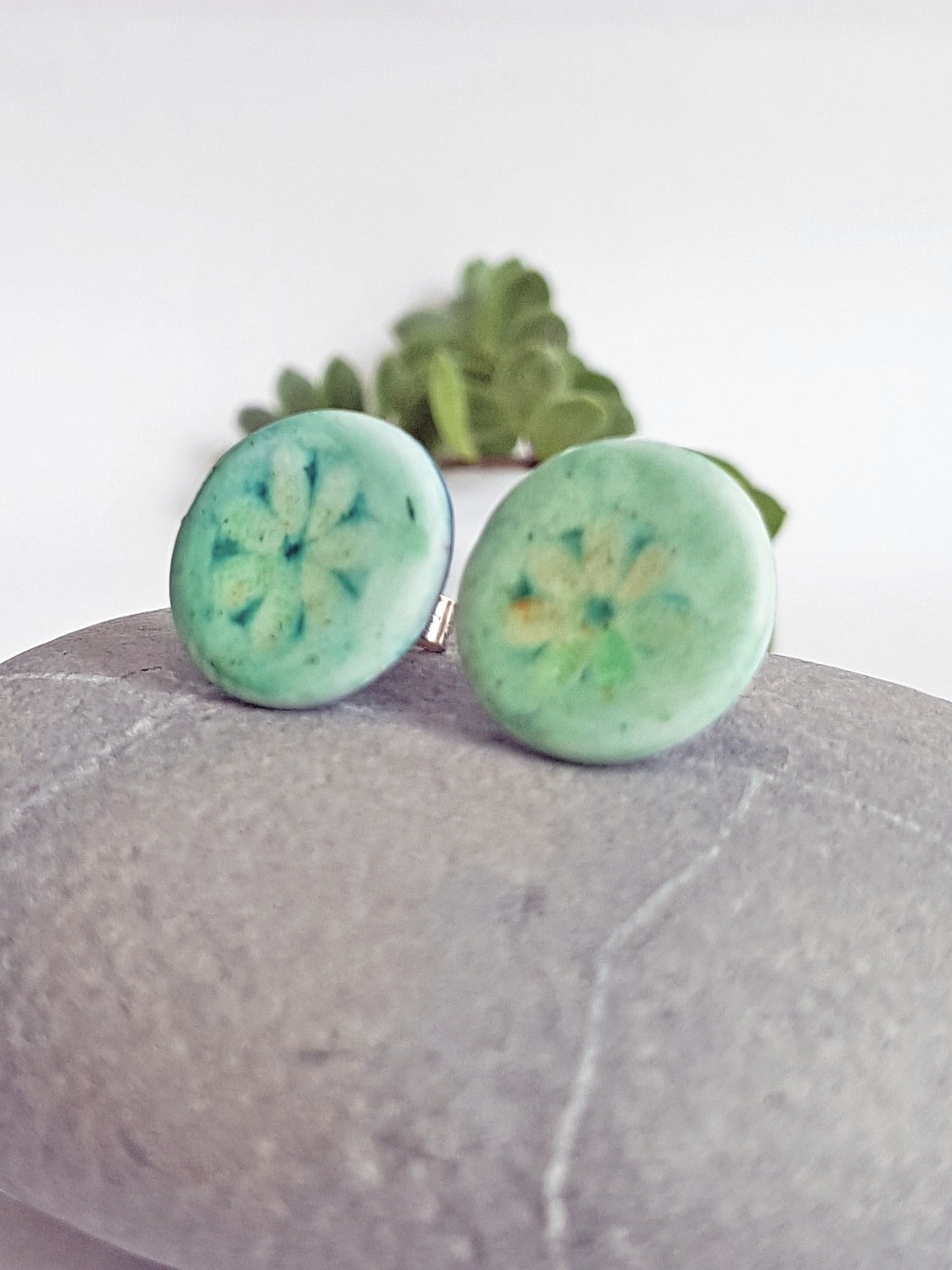 Side of round polymer clay stud earring with turquoise faded daisy motif.