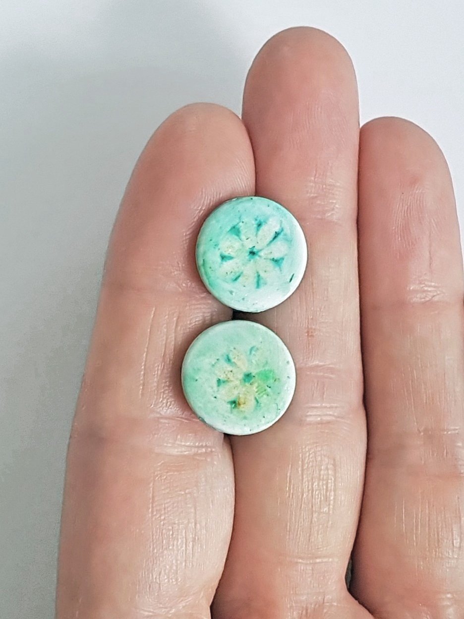 15 mm round Kalamata stud earrings held between two fingers to indicate scale