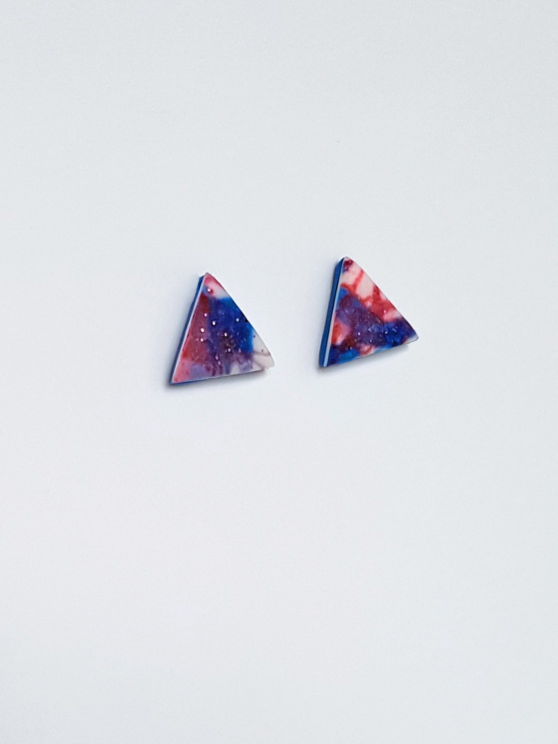 Handcrafted polymer clay stud earrings with a finely detailed abstract line and brushstroke pattern in dark red, white and electric blue.