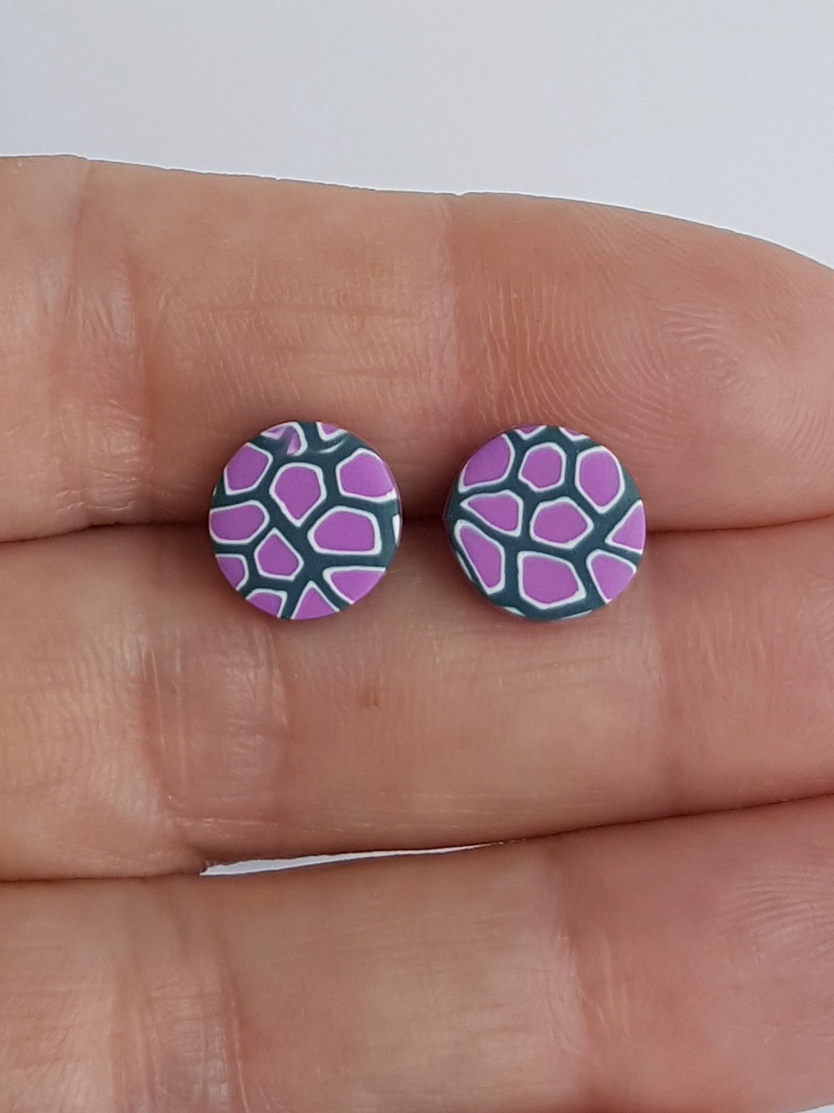 Lilac, white and grey round studs held between fingers to indicate size.