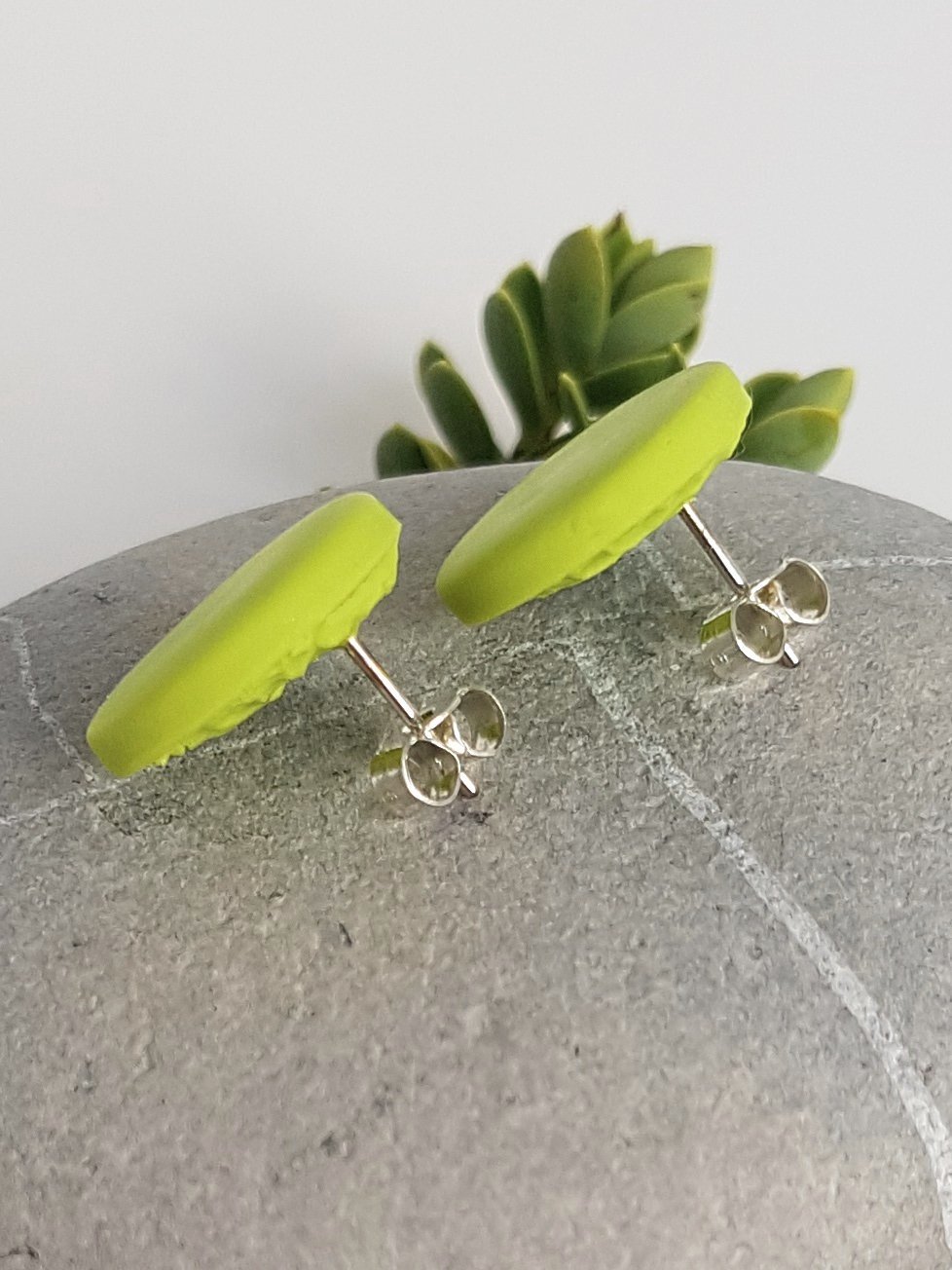 Lime green round polymer clay stud earrings with lightly textured backs and sterling silver posts and scrolls.