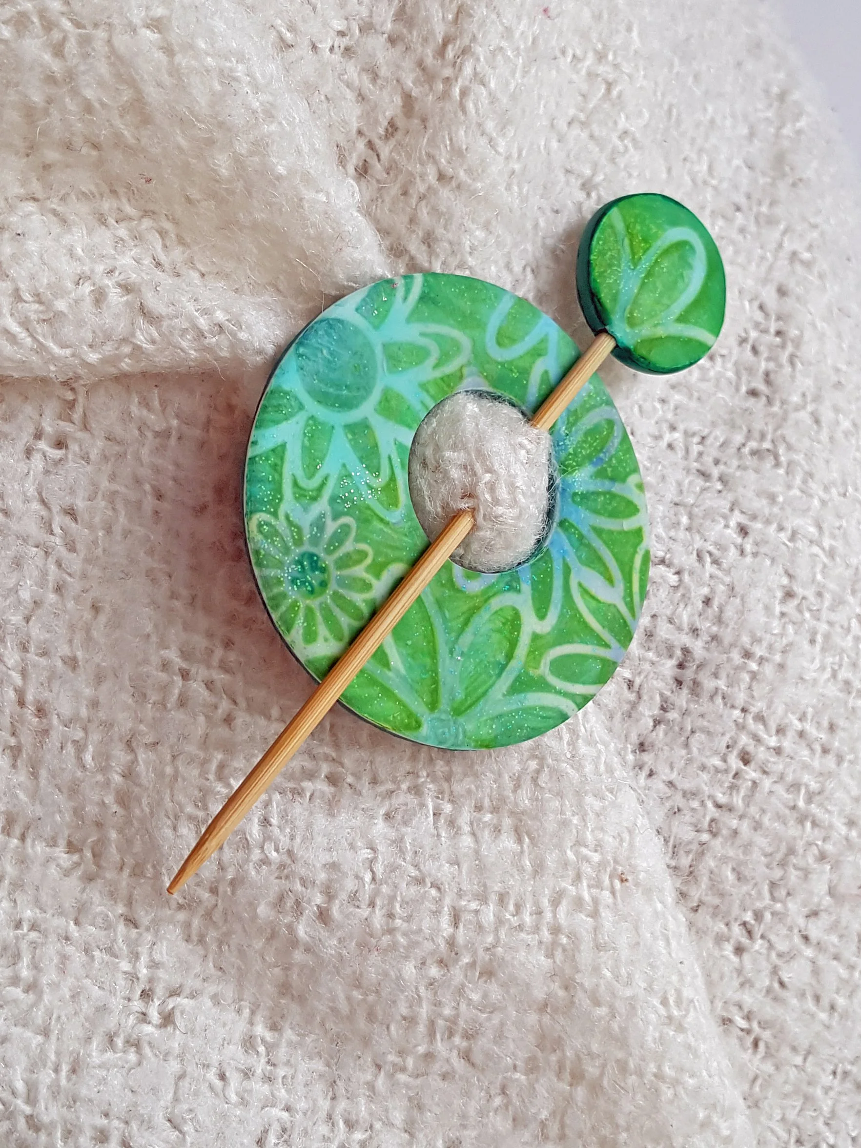 Shades of pale blue and leaf green with a white outline stylised daisy design decorates polymer clay disc and bamboo shawl pin.